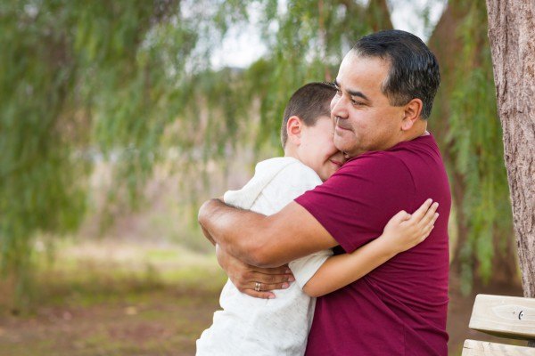Foto de pai e filho se abraçando em uma praça.