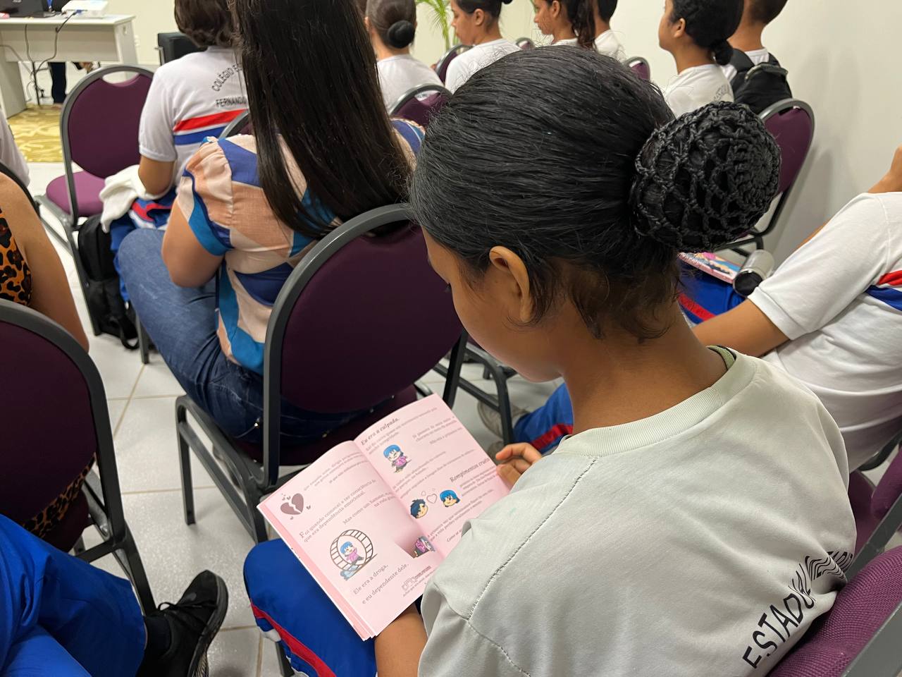 Foto colorida mostra uma estudante lendo a cartilha "Estou namorando e agora" do TJRR