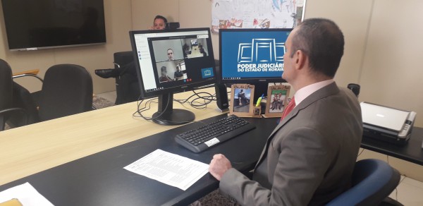 Juiz Air Marin no gabinete iniciando a videoconferência com auxílio de um computador, internet e uma câmera  