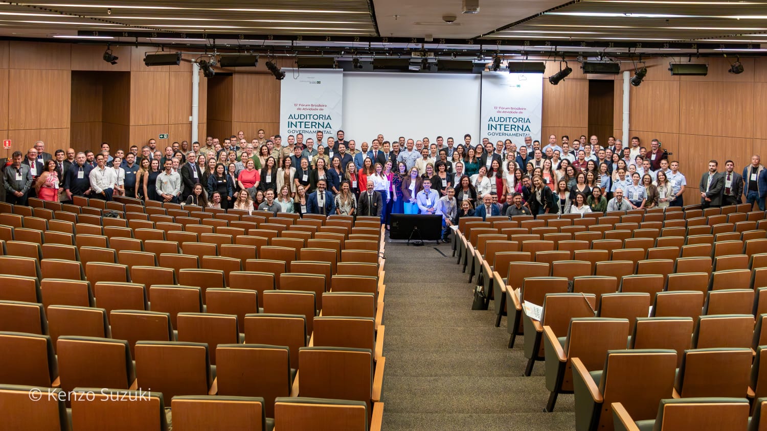 imagem ampla mostra um grupo de pessoas em um auditório pousando para fotografia