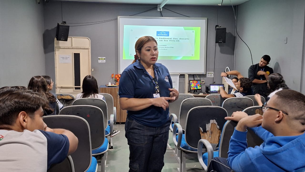 foto colorida de uma servidora da ouvidoria realizando uma palestra em um auditório pequeno