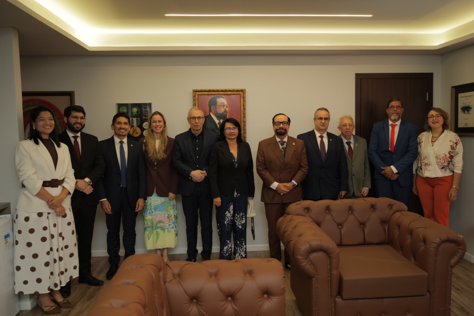 Imagem colorida mostra representantes do Judiciário e de instituições parceiras posando para foto após a programação. O grupo aparece reunido em uma sala institucional, diante de obras e quadros decorativos.