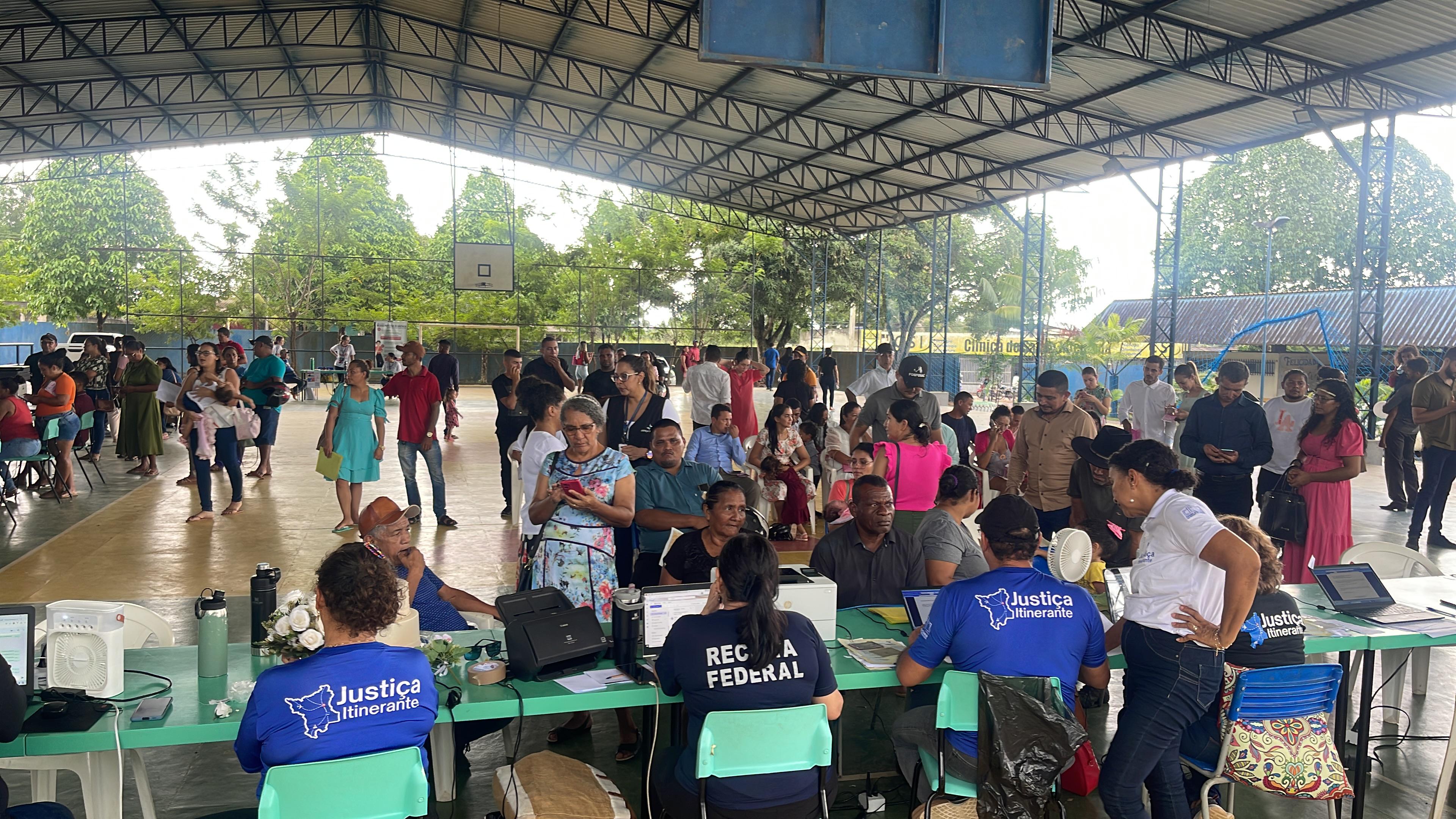 Imagem colorida do atendimento da Vara da Justiça Itinerante. A imagem mostra um ginasio cheio de pessoas esperando pelo atendimento da Itinerante
