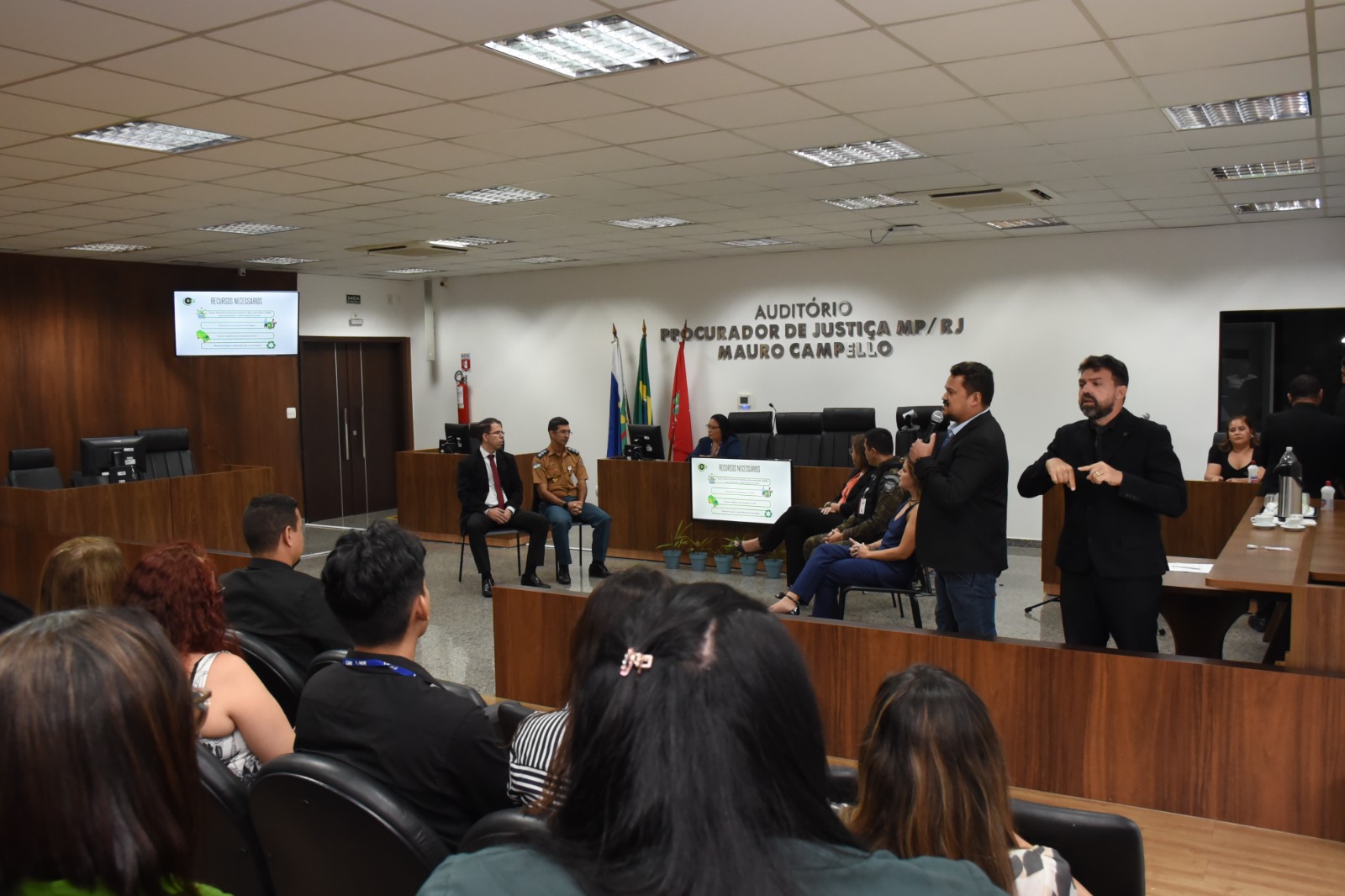 Imagem colorida mostrando pessoas sentadas em um auditório durante evento
