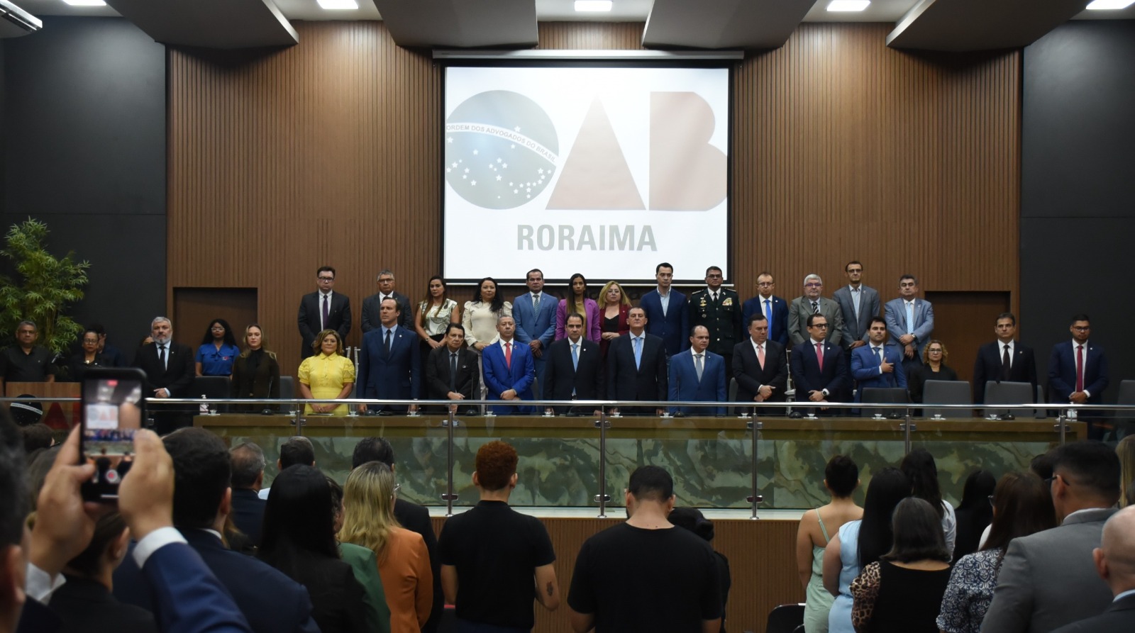 Imagem colorida mostrando uma mesa de autoridades em pé durante evento