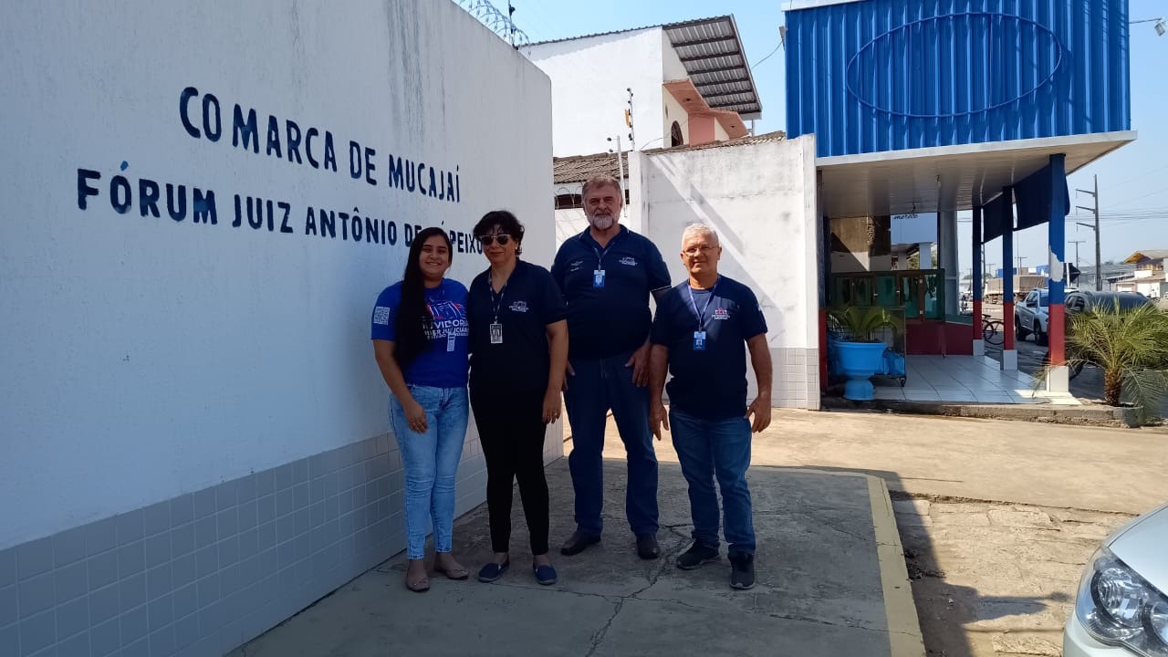 foto colorida de servidores da ouvidoria do Tjrr pousando para fotografia enfrente do letreiro escrito no muro " comarca de mucajaí"