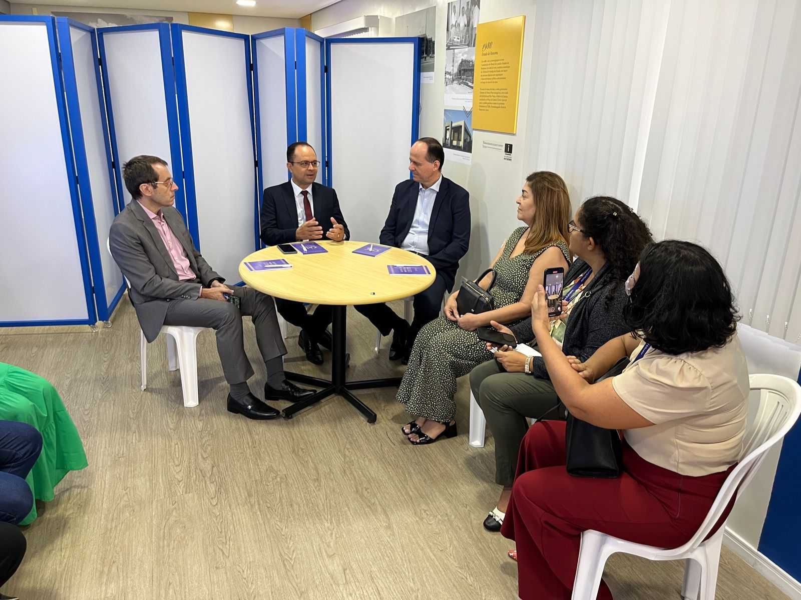 Foto colorida , com seis pessoas sentadas em volta de uma mesa, conversando