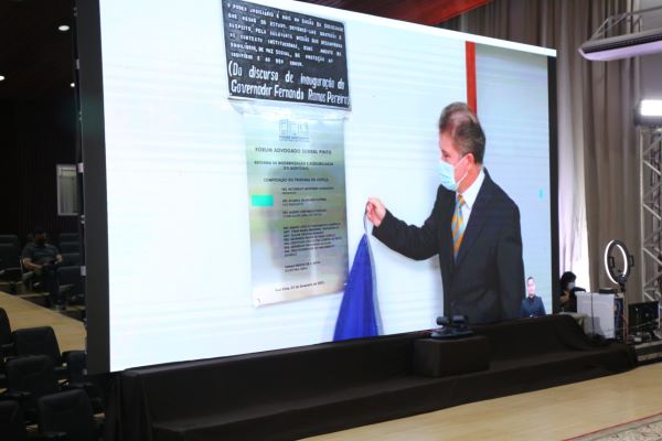 Foto com imagem da tela de projeção em cima do palco, que mostra Desembargador e placa do Fórum Advogado Sobral Pinto.
