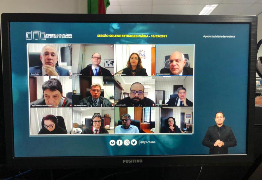 Foto de tela de computador, mostrando a sessão solene virtual, nela aparecem os desembargadores participando por videoconferência e o intérprete de libras.