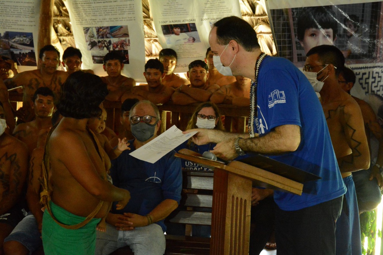 Presidente do TJRR, Desembargador Cristóvão Suter entregando a certidão de nascimento da última criança nascida na comunidade, Kipná Genilson Atroari.