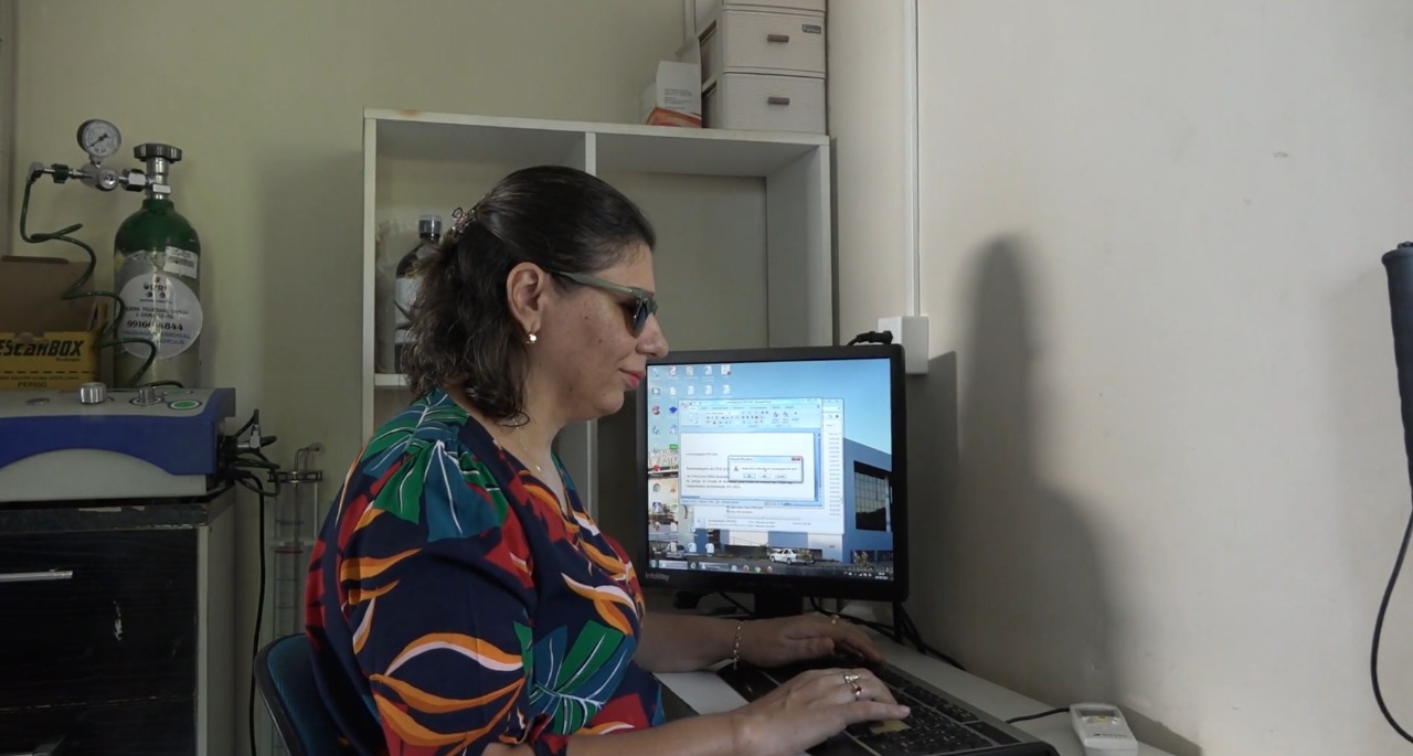 A servidora Vera Sábio, membro da Comissão de Acessibilidade, será uma das participantes da dinâmica. Na imagem ela aparece em home office, sentada em uma mesa com um teclado e um monitor ao seu lado. Ela é uma mulher de meia idade, de cabelos escuros e curtos, usa óculos escuros e traja roupa estampada. 