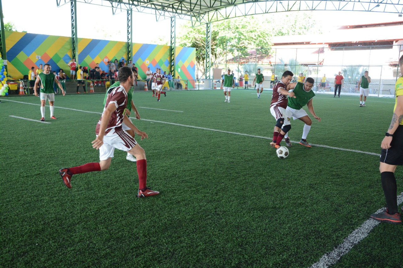 Imagem colorida contém times I FutJus jogando futebol society no gramado sintético do complexo Ayrton Senna.