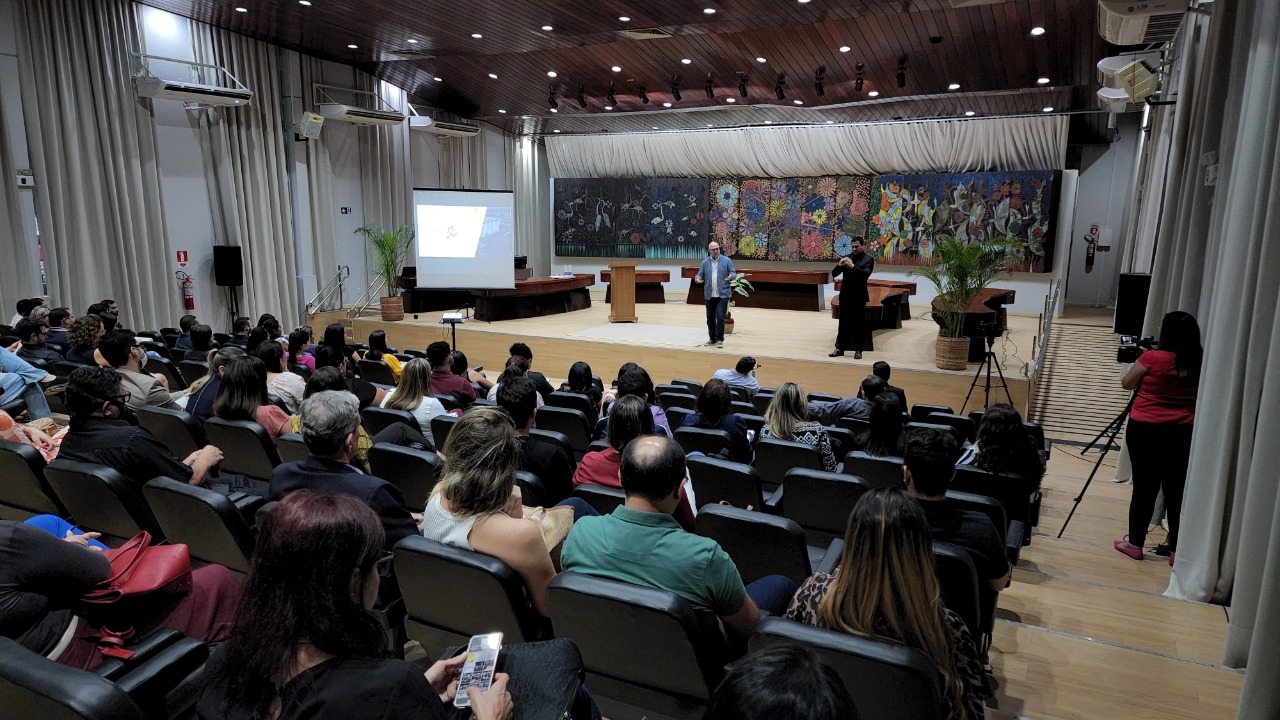 oto colorida mostra pessoas sentadas nas poltronas do auditório do Fórum Advogado Sobral Pinto, durante a palestra do Eduardo Sabbag. No palco está o palestrante e ao lado um intérprete de libras. 