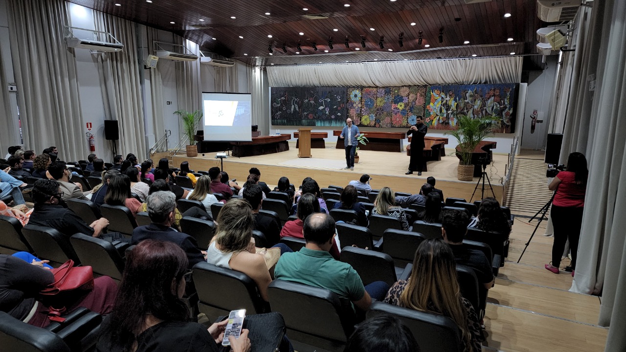 oto colorida mostra pessoas sentadas nas poltronas do auditório do Fórum Advogado Sobral Pinto, durante a palestra do Eduardo Sabbag. No palco está o palestrante e ao lado um intérprete de libras.