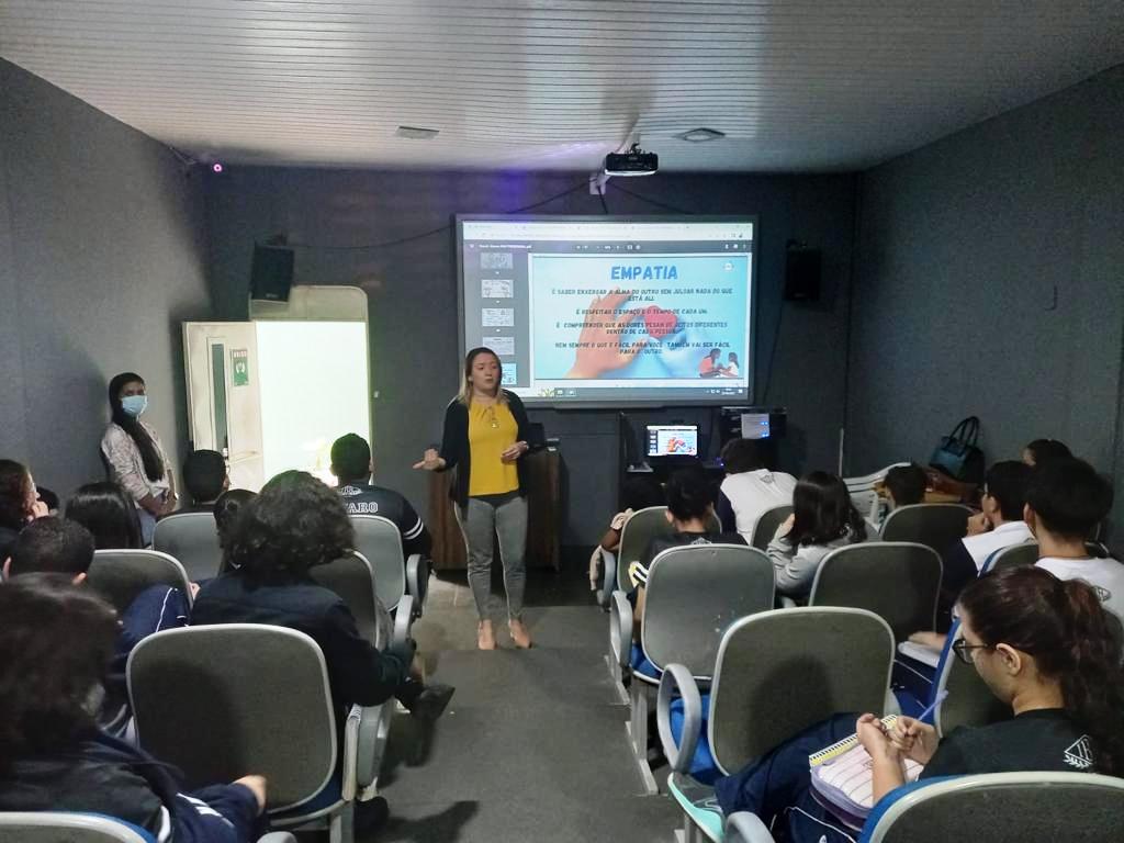 A imagem mostra uma sala com adolescentes sentados em cadeiras assistindo a uma palestra do programa Justiça Comunitária. 