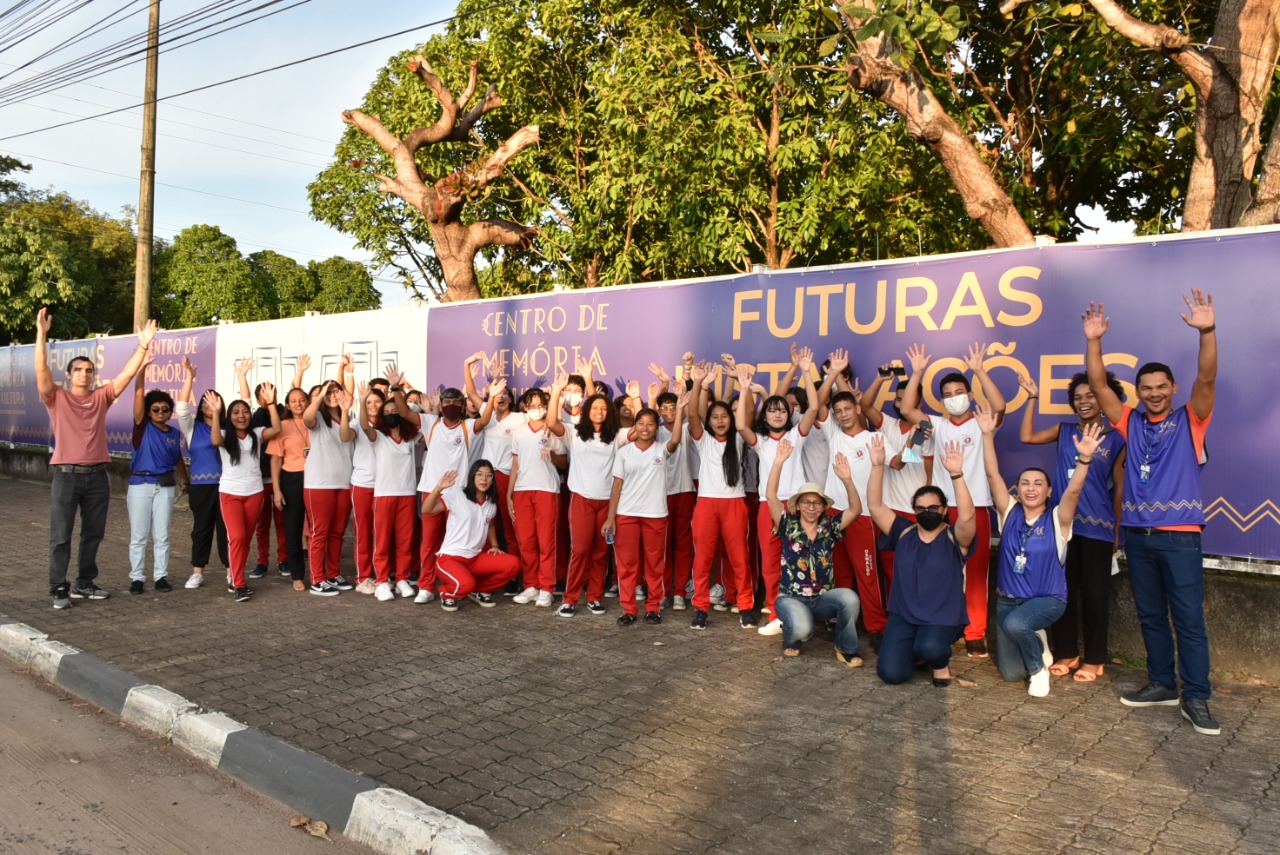 Imagem colorida contém alunos da Escola Estadual Oswaldo Cruz  e servidores do TJRR, em frente ao banner do Centro de Memória do TJRR. 