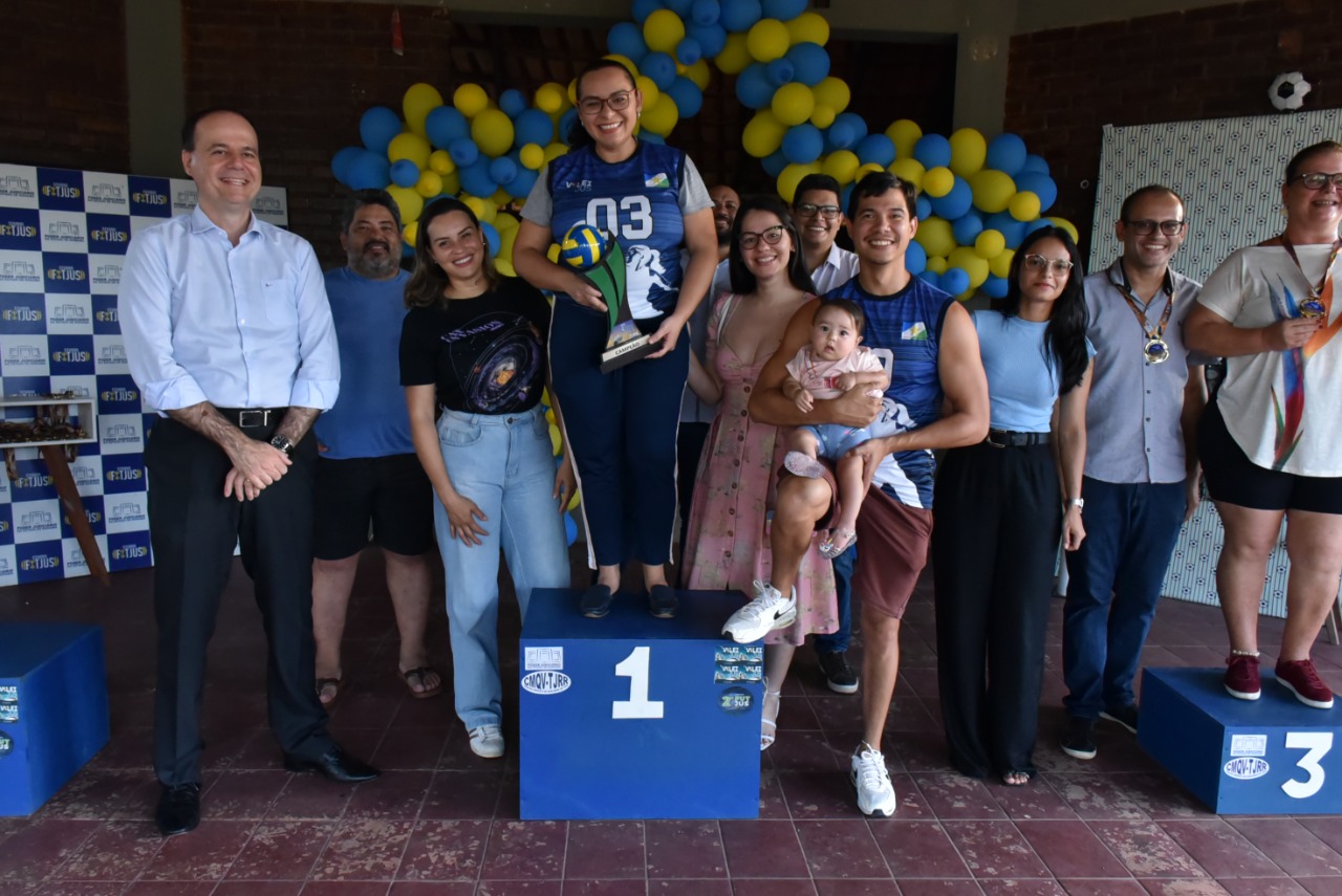 Imagem colorida contém participantes dos torneios Futjus e voleijus posando para fotografia no pódio de primeiro lugar ao lado do presidente do TJRR, desembargador Cristóvão Súter. Na imagem, um dos participantes segura uma criança de colo nos braços.