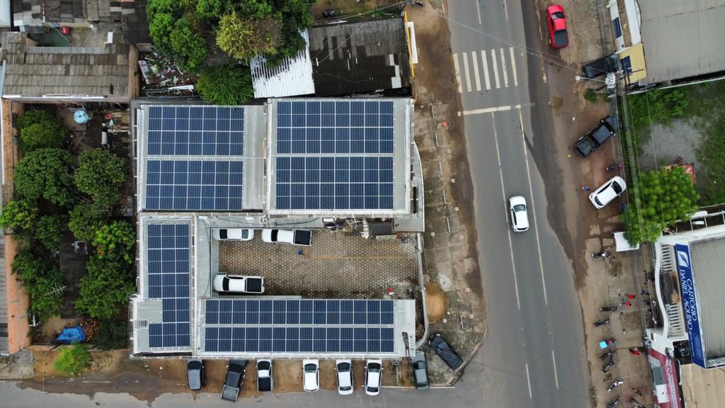  Imagem aérea colorida em um formato retangular, mostrando o  teto da 1ª e 2ª Varas da Infância com uma pequena área com vegetação, além de uma via de trânsito com um carro em movimento e alguns  estacionados.