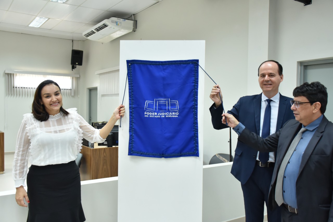 Imagem colorida mostra Juíza titular da Comarca de Caracaraí, Noêmia Cardoso, o  presidente TJRR, desembargador Cristóvão Suter e o vice presidente do TJRR, Desembargador Jésus Nascimento, sorridentes segurando o fio da faixa de inauguração.