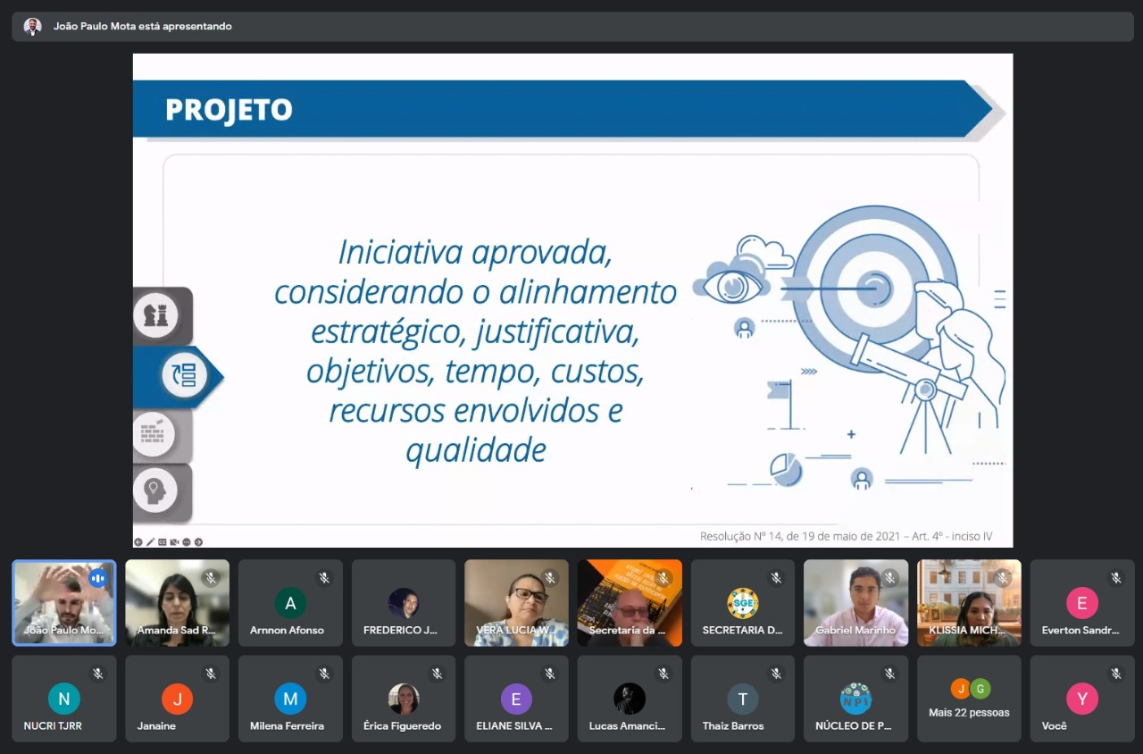  Imagem colorida em formato retangular mostra um sala virtual com 20 participantes. Ao centro da imagem está sendo apresentado um slide com o texto “Projeto - Iniciativa aprovada, considerando o alinhamento estratégico, justificativa, objetivos, tempo, custos, recursos envolvidos e qualidade”.