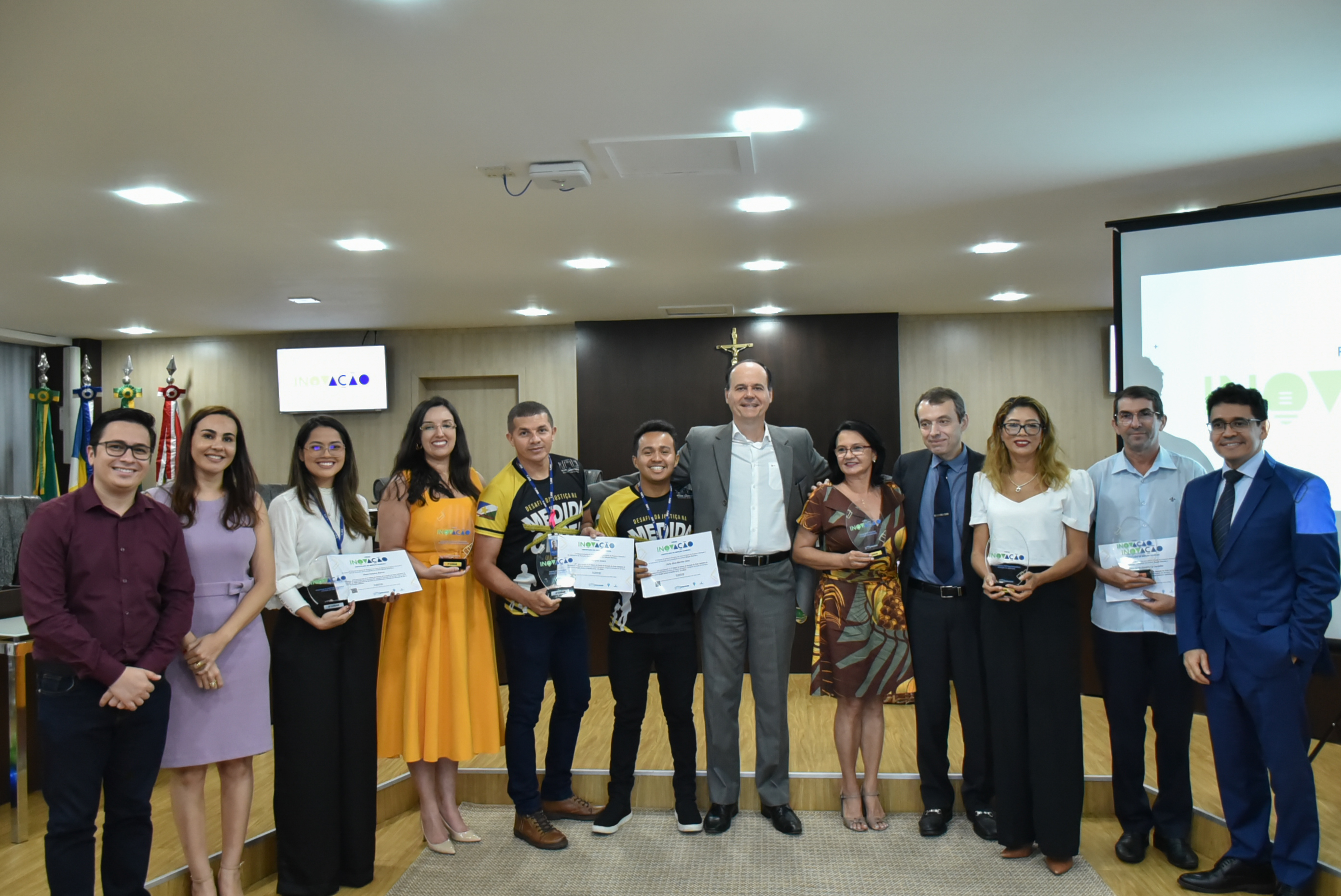 Imagem colorida em formato retangular mostra os vencedores do 1º Prêmio de Inovação do Poder Judiciário de Roraima com seus troféus e certificados em mãos,  entre eles, localizado no centro da foto está o presidente do TJRR, desembargador Cristóvão Suter.