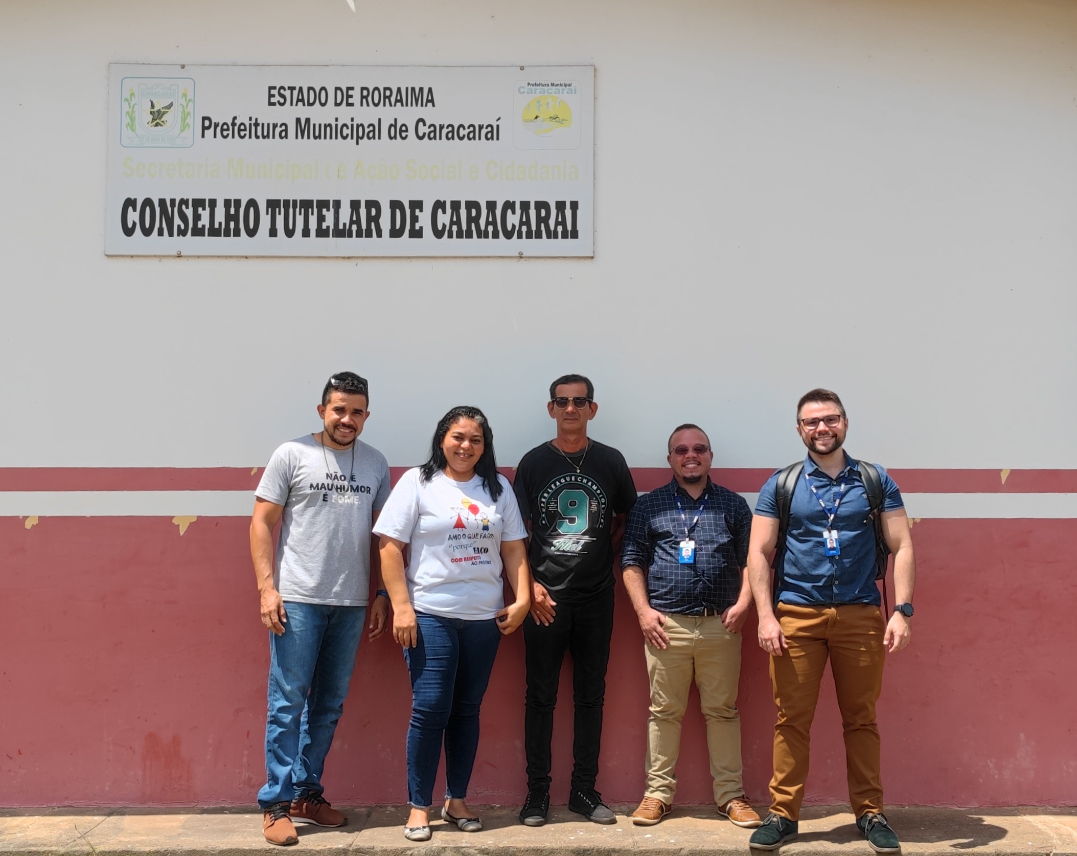 imagem colorida em formato quadrado mostra quatro homens e uma mulher em pé posando para na frente da placa do conselho tutelar de Caracaraí.