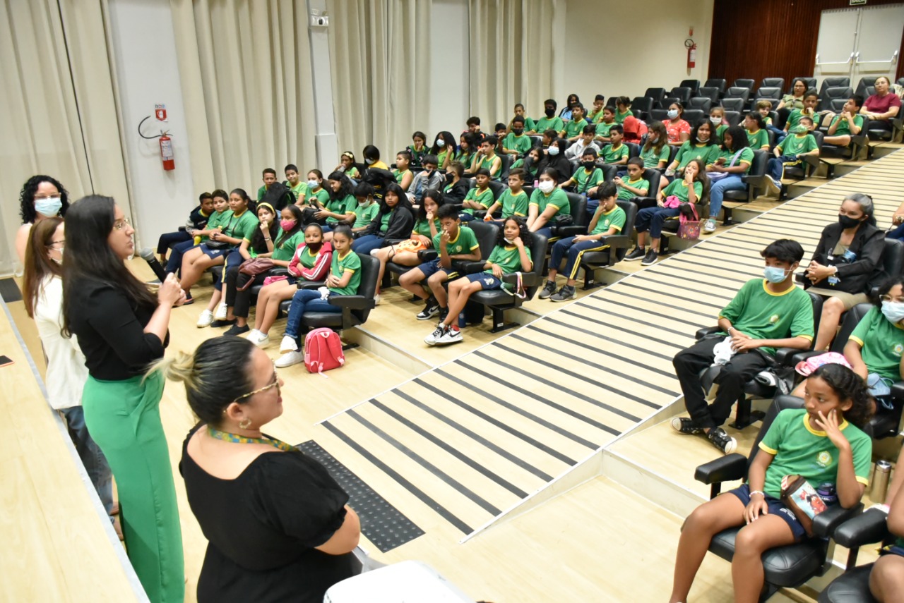 Imagem colorida em formato retangular mostra alunos e alunas fardados, sentados no auditório do Fórum Cível Advogado Sobral Pinto, à frente está a coordenadora da Cevid , juíza Suelen Alves e a secretária Adjunta Pedagógica, Meiry Jane Silva acompanhadas de duas professoras, conversando com os alunos e alunas presente no local.