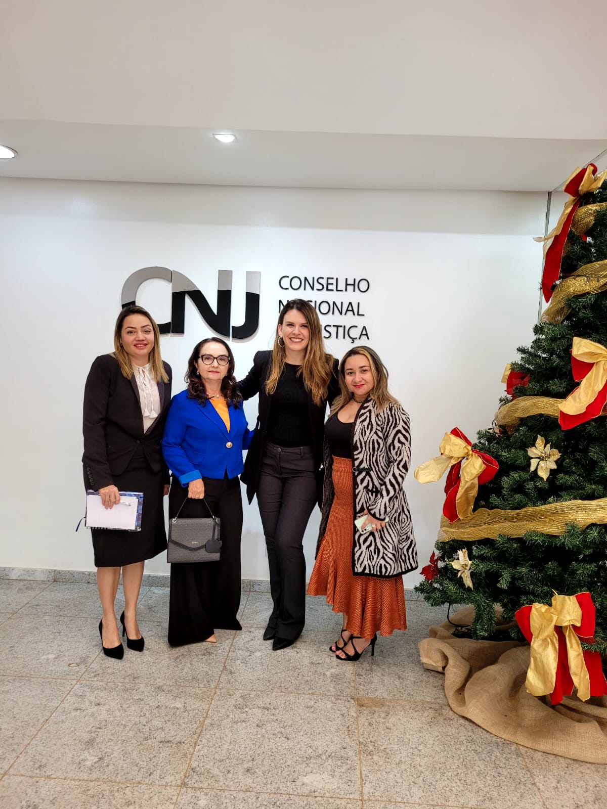 Imagem colorida em formato retangular, mostra as servidoras do cerimonial do Tribunal de Justiça de Roraima (TJRR), Haline Barreto, Domícia Marques e Solange Alencar, posando para a foto com representante das Secretarias de Cerimonial do Conselho Nacional de Justiça.