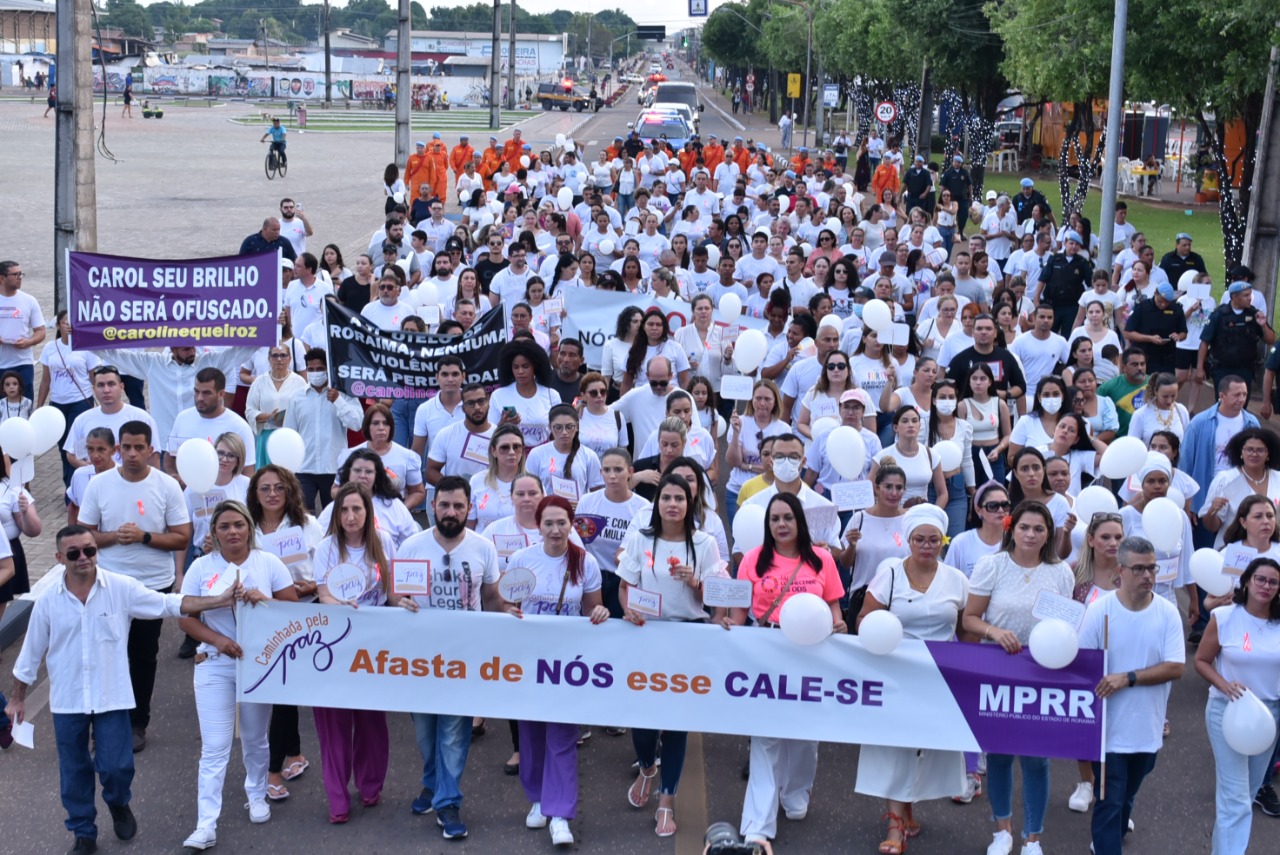 Imagem colorida em formato retangular, mostra homens e mulheres vestidos de branco e segurando cartazes durante caminhada pela paz, o cartaz principal apresenta o texto “caminhada pela paz, Afasta- se de nós esse cale-se, MPRR”