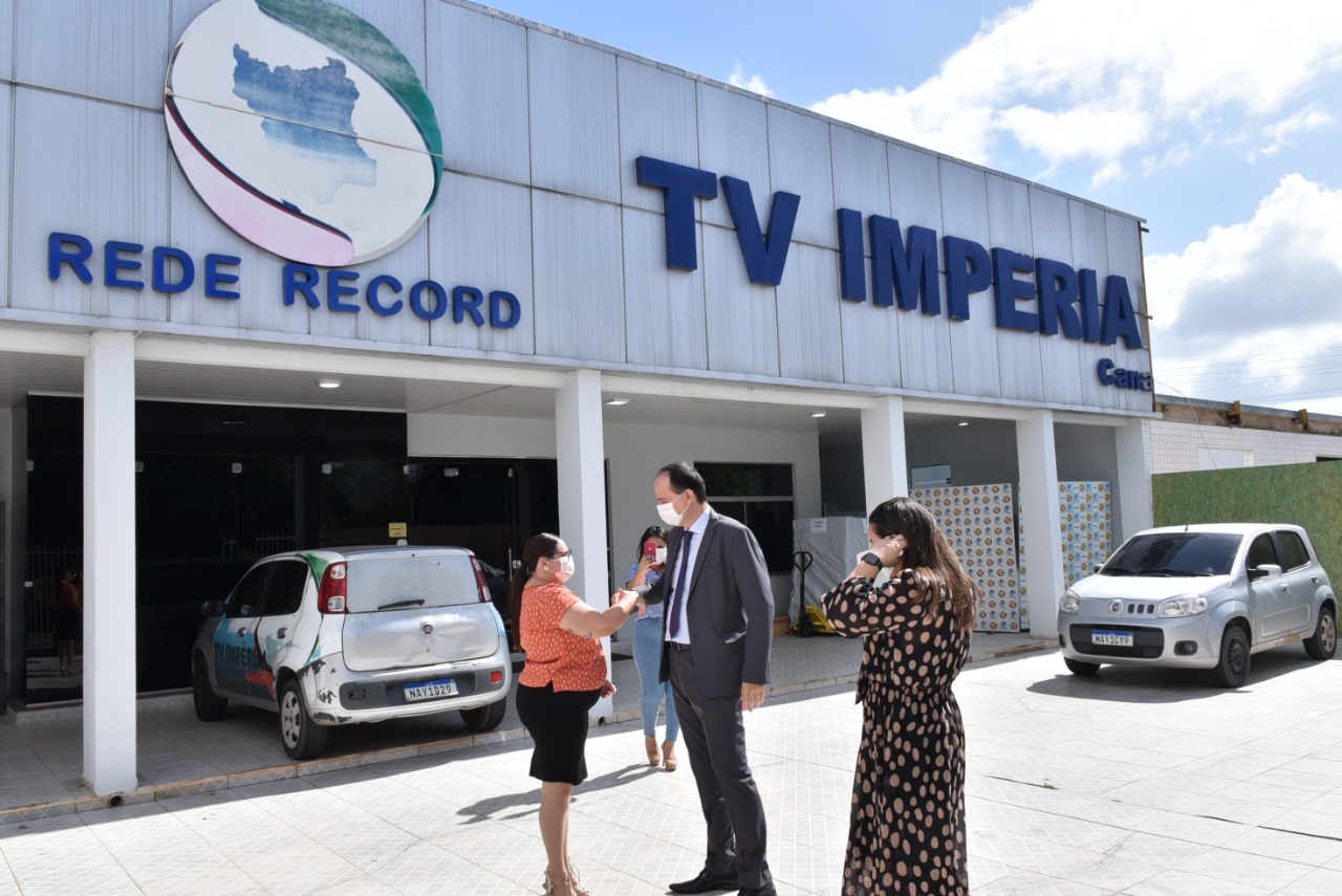 Imagem colorida em formato retangular mostra  o presidente do Tribunal de Justiça de Roraima, desembargador Cristóvão Suter, cumprimentando uma mulher em frente a TV Imperial, filial da Rede Record.