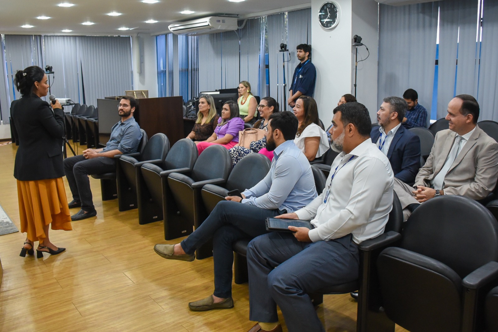 Imagem colorida em formato retangular mostra a Secretária de Gestão Estratégica (SGE), Veruska Lobo, discursando em pé com o microfone na mão para o presidente do Tribunal de Justiça de Roraima (TJRR), desembargador Cristóvão Suter, secretários e coordenadores da instituição que estão sentados no auditório da Sala de Sessões do Palácio da Justiça.