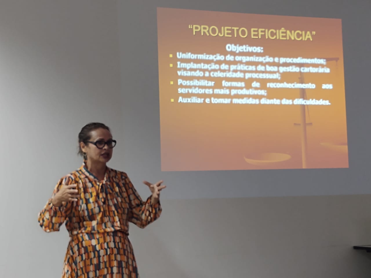 Imagem colorida em formato retangular mostra a juíza titular da Vara da Justiça Itinerante do Tribunal de Justiça de Roraima (TJRR), Graciete Sotto Mayor Ribeiro, em pé à frente de uma tela de projeção exibindo um slide.