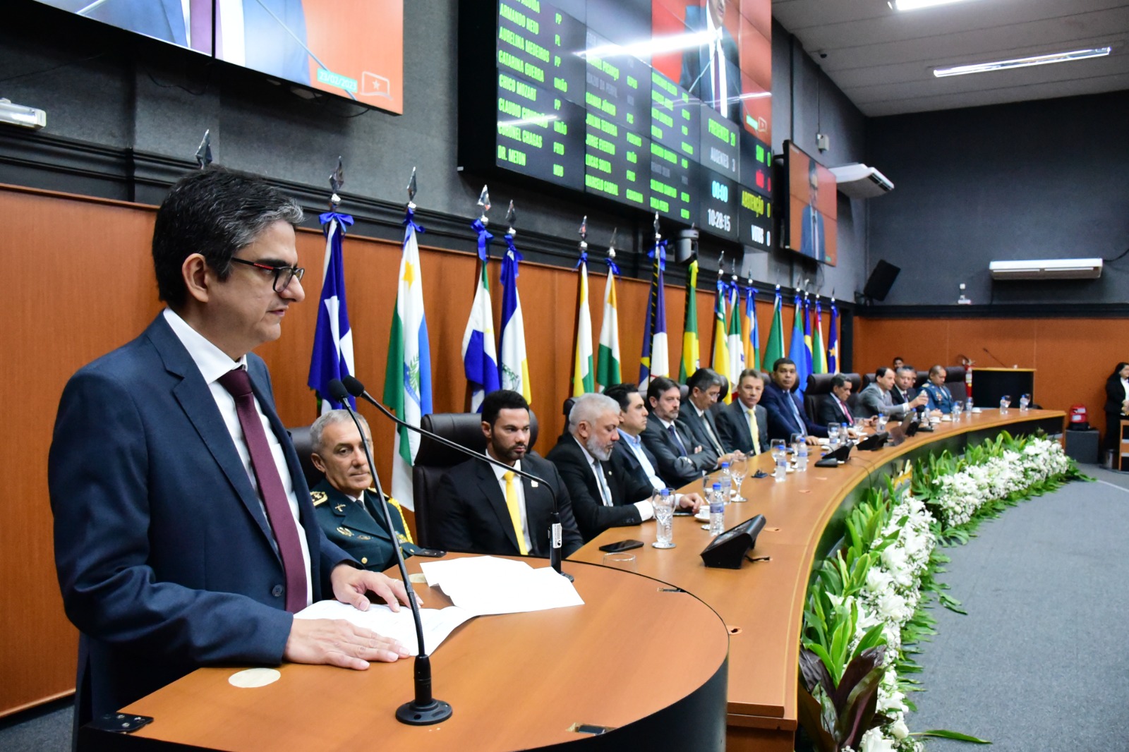Imagem colorida mostra o desembargador Ricardo Oliveira, durante o discurso de solenidade de instalação da primeira sessão legislativa. Ao fundo as autoridades sentaram-se à mesa de honra no Plenário da ALE-RR.
