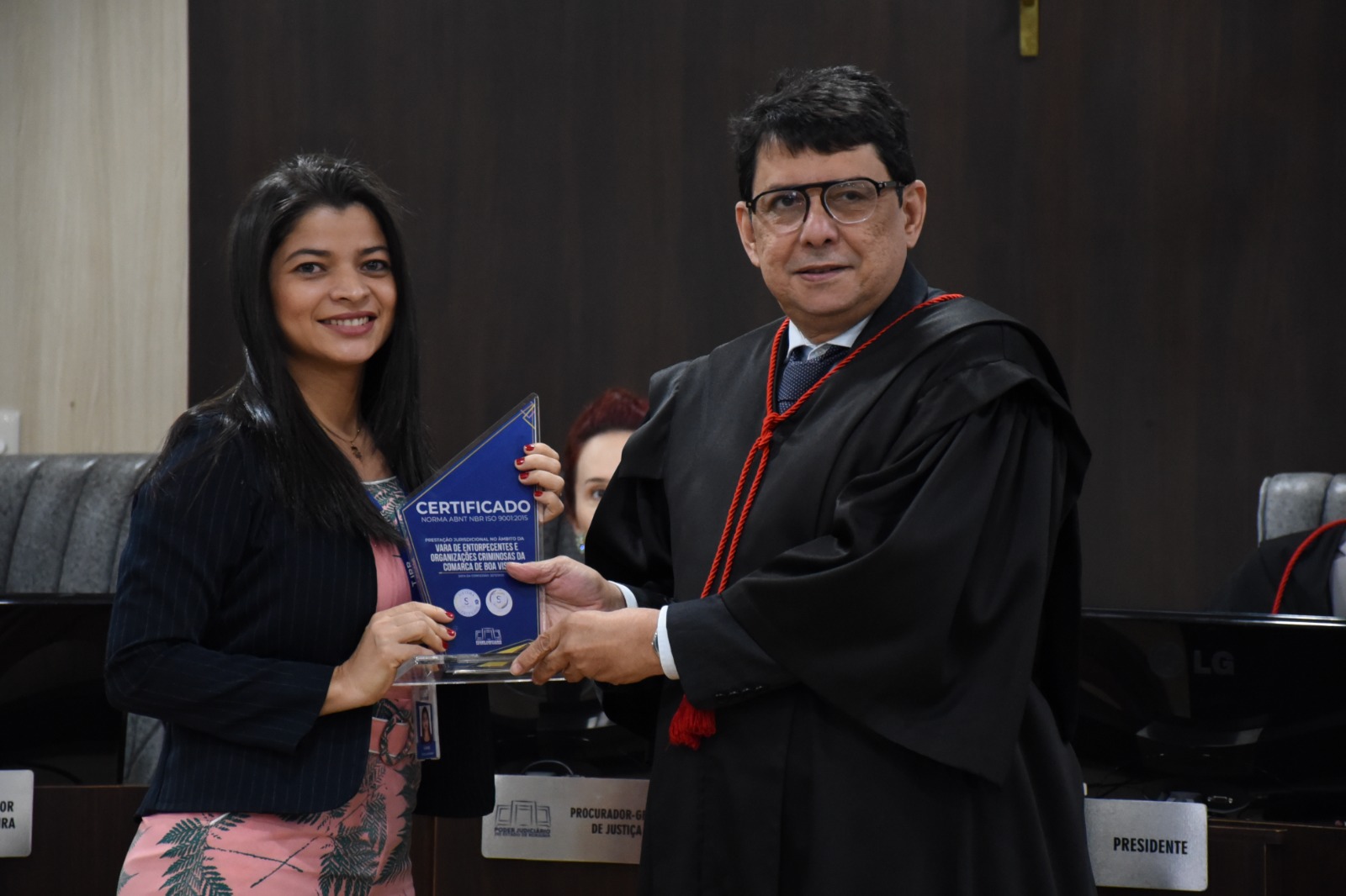 Imagem  colorida mostra o desembargador Jesus Nascimento, posando para a foto ao lado de uma servidora do Tribunal, ambos seguram o troféu certificado de qualidade de serviços prestados.