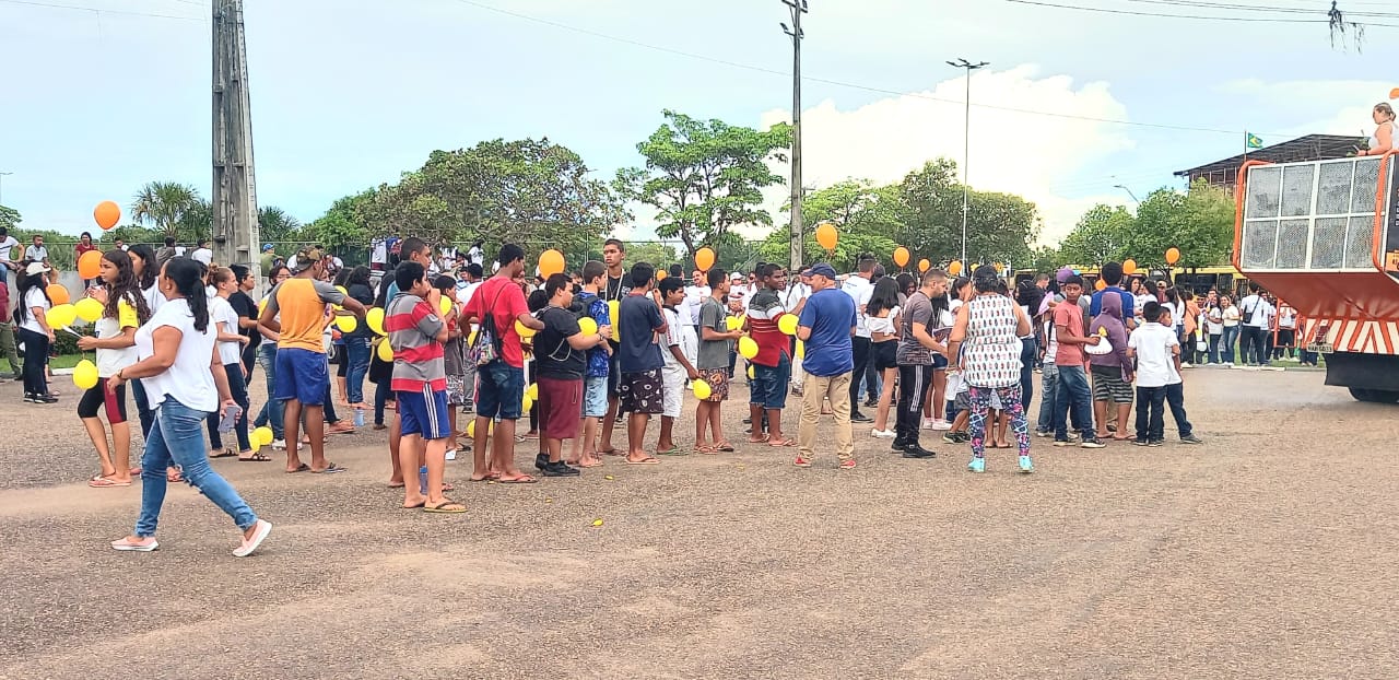 Imagem colorida mostra um aglomerado de pessoas reunidas segurando balões amarelos.