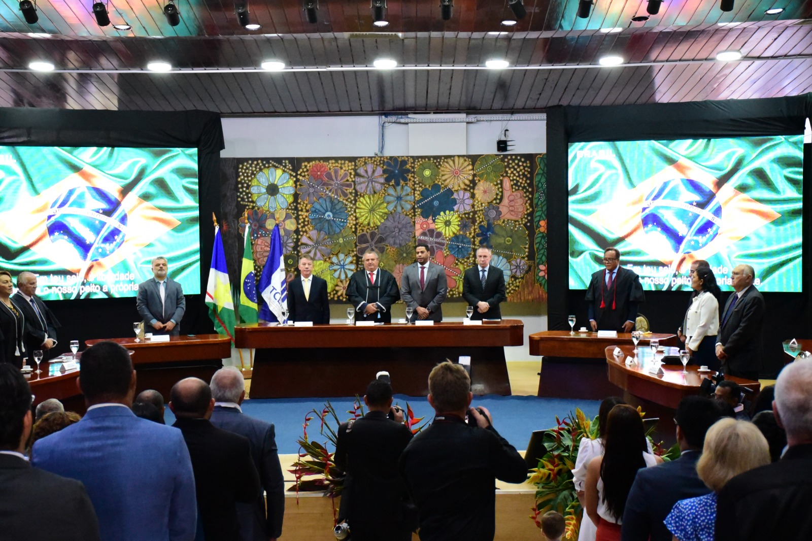 Foto mostra parte da mesa de autoridades. Todos estão posicionados próximo da mesa, de pé. Da esquerda para a direita: o governador Antonio Denarium, de terno e gravata amarela, o conselheiro Célio Wanderley, de terno e toga, o deputado federal Jhonatan de Jesus, de terno cinza e gravata vermelha, e o desembargador Almiro Padilha, de terno e gravata escuros.