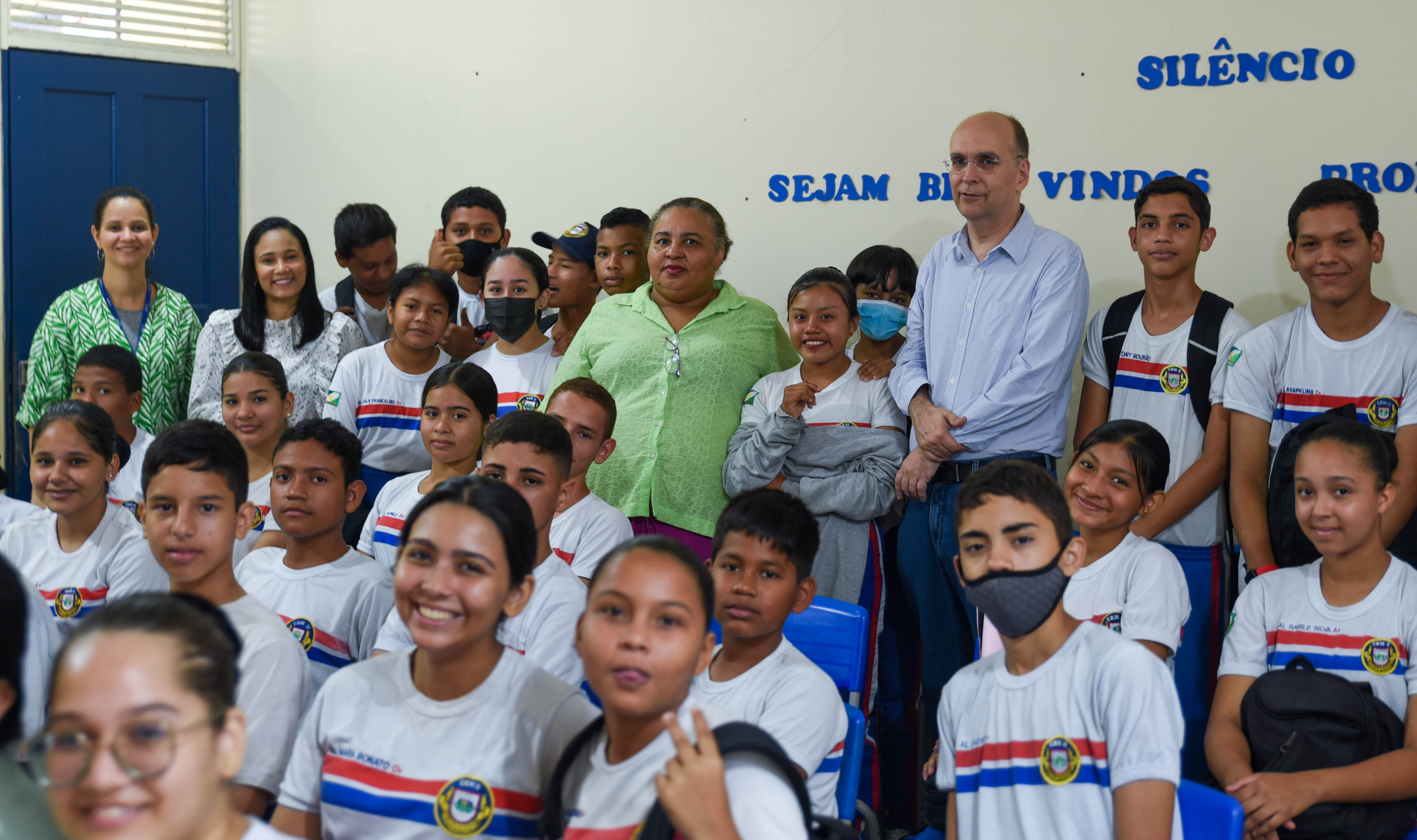 Imagem colorida mostra o juiz em pé, posando para a foto ao lado da gestora da escola, Angela Maria Leite, de duas colaboradoras do TJRR e dos estudantes da Escola Estadual Luiz Rittler Brito de Lucena.