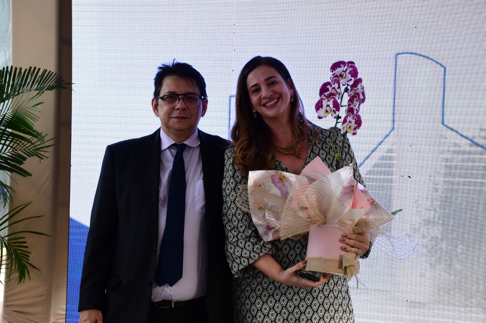 Emira Latife Salomão é neta de Latife Salomão,ao lado do Presidente do TJRR, des Jésus Nascimento pousando para a foto com flores em homenagem em nome da avó.