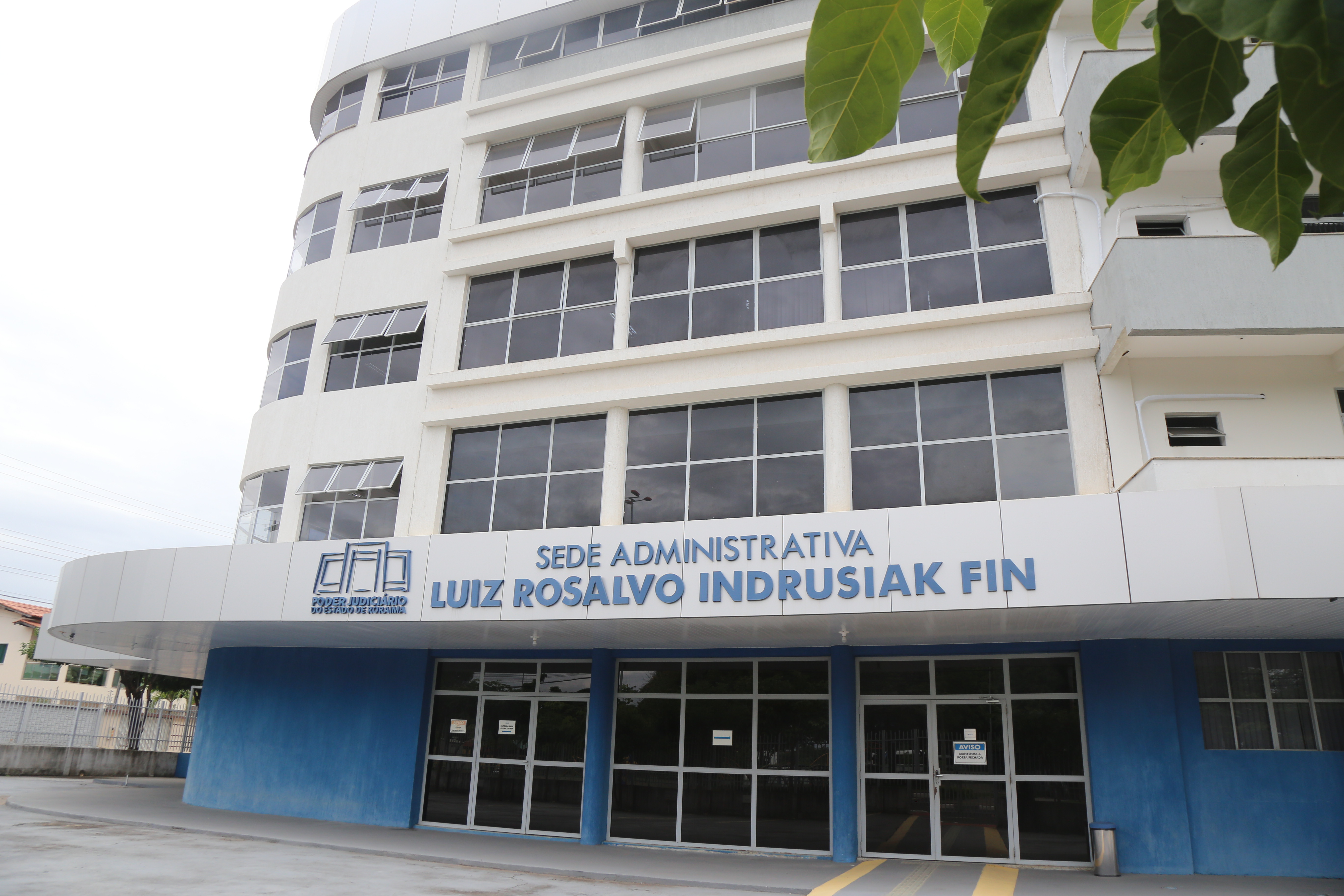 Foto colorida mostra a fachada da Sede Administrativa Luiz Rosalvo Indrusiak Fin, do Poder Judiciário de Roraima. O prédio possui quatro andares e possui as cores branca e azul.