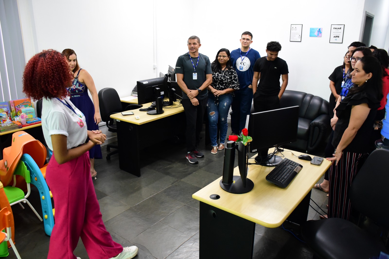 Foto mostra servidora do TJRR repassando orientações para outros servidores, que observam atentos, dentro de um espaço de trabalho onde existem estações e computadores.