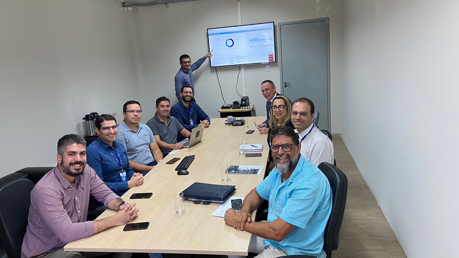 foto colorida em um sala de reunião sentados ao redor da mesa e olhando para a fotografia 