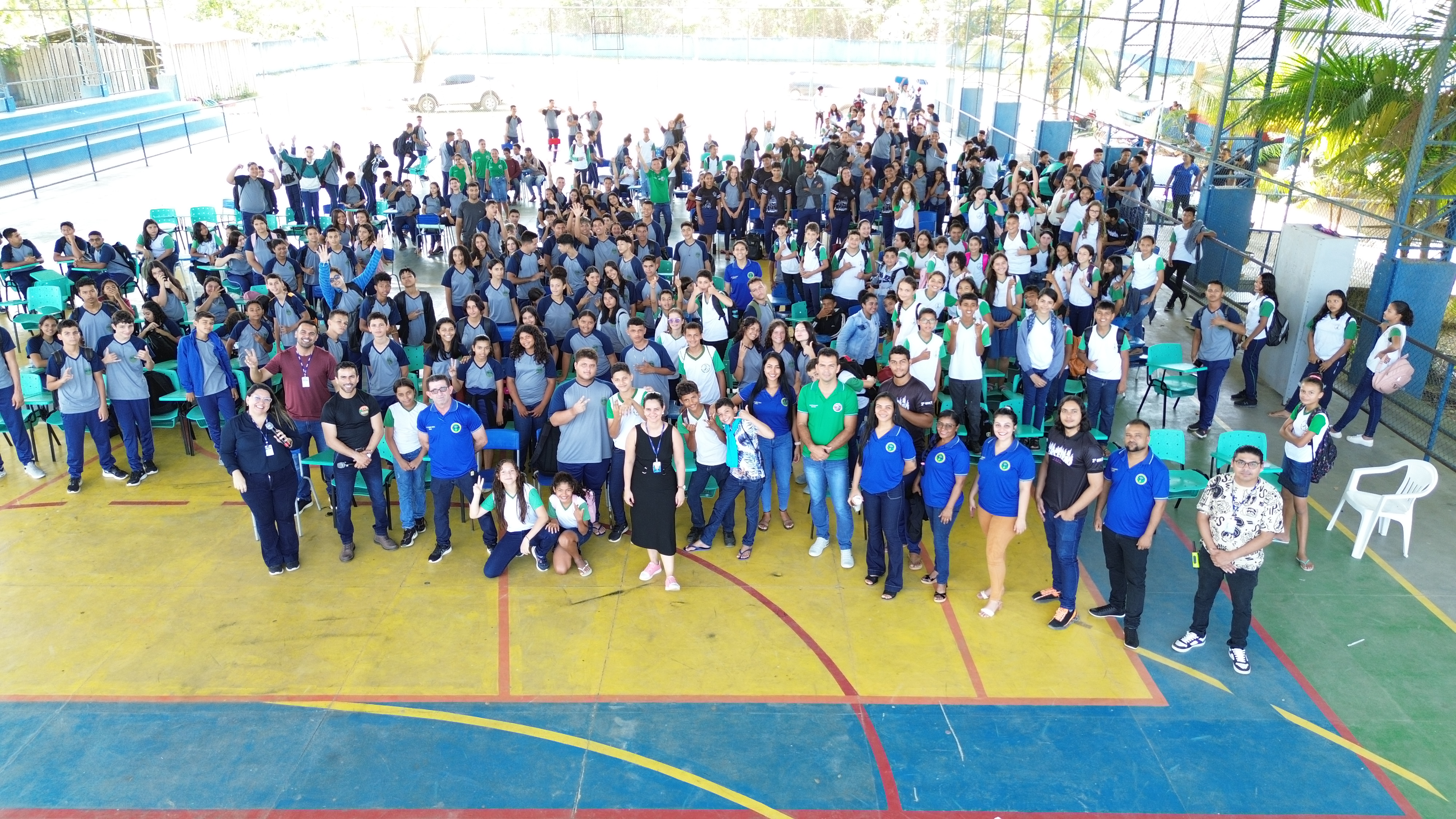 Foto colorida tirada em drone de uma quadra cheia de alunos reunidos em pé e pousando para a fotografica