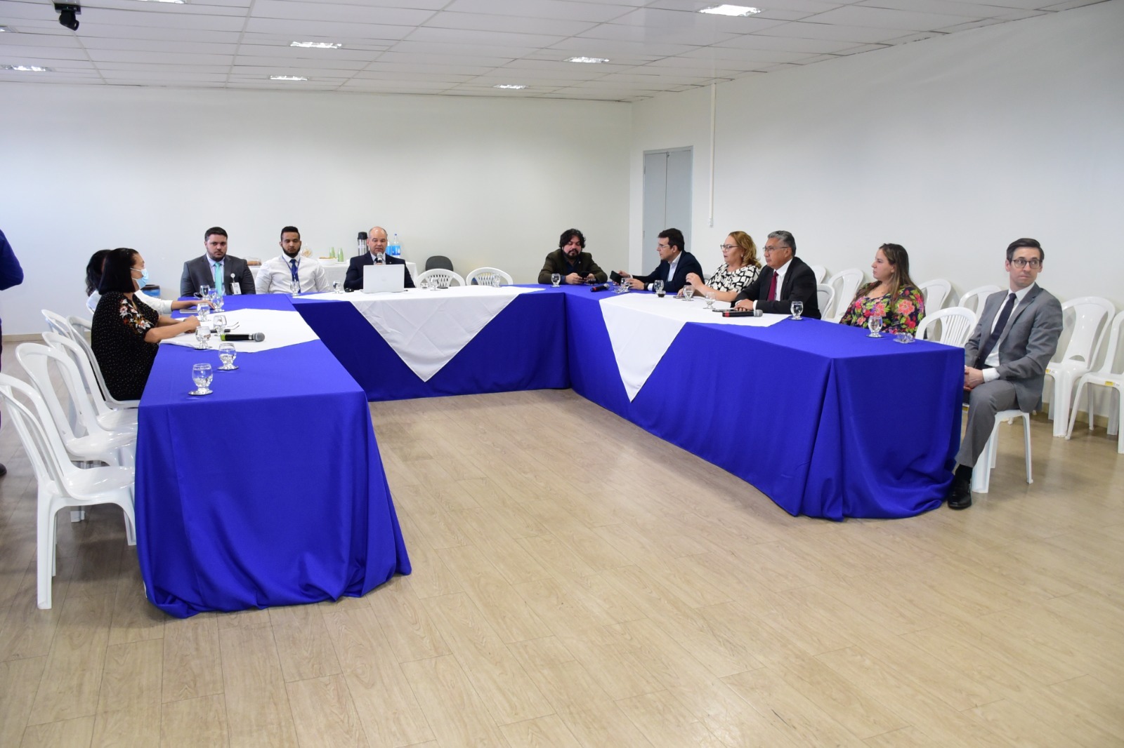 foto colorida com autoridades sentados em uma mesa que está em formato de C e com toalhas azul e brancas ao meio