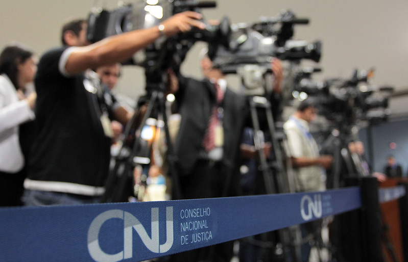 foto colorida dando enfoque em fita do CNJ e ao fundo com desfoque está cinegrafistas