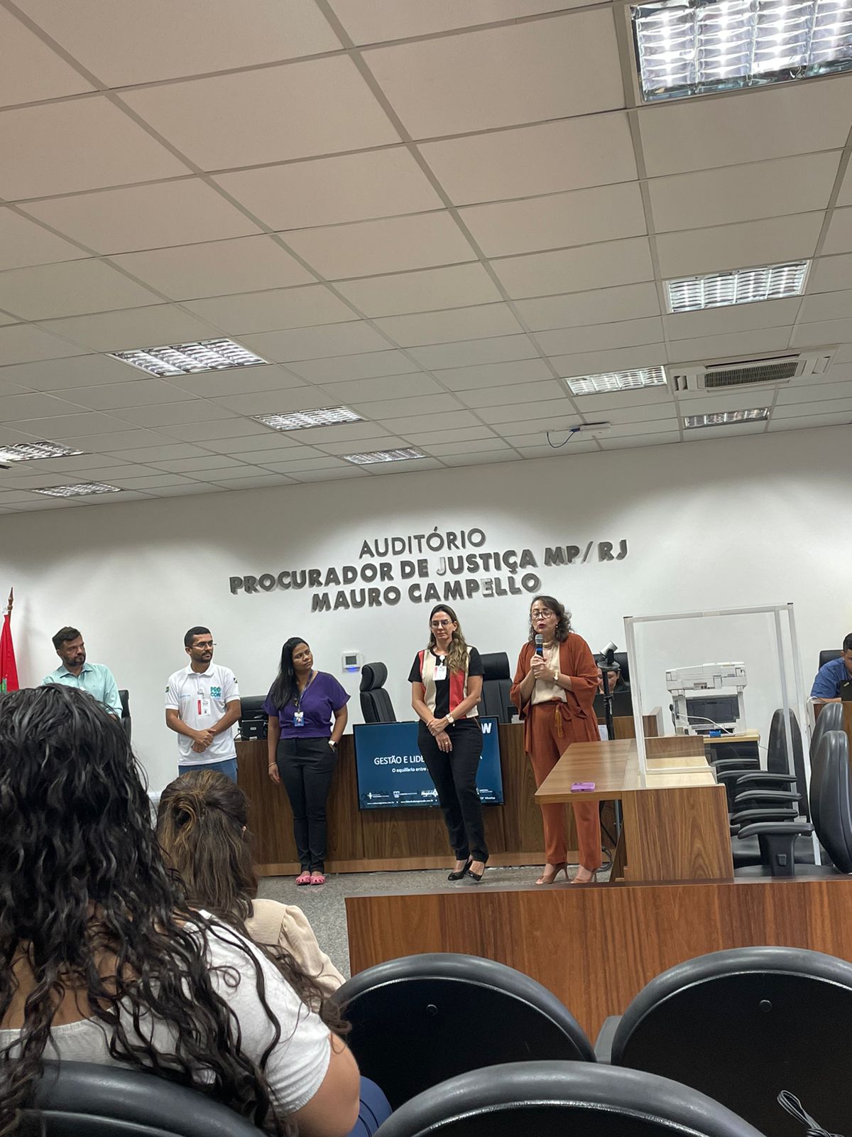 foto colorida mostra a diretora do Fórum Criminal Ministro Evandro Lins e Silva, juíza Lana Leitão, ao lado da reitora do Centro Universitário Estácio da Amazônia, Brena Linhares, da psicóloga do TJRR, Perla Lima, do Secretário de Comunicação do Estado de Roraima, Weber Negreiros, do tradutor de libras e do servidor do Procon, durante abertura da “Ação Cuidando do Servidor”, que ocorreu no no Auditório Procurador de Justiça MP/RJ Mauro Campello, do Fórum Criminal Ministro Evandro Lins e Silva do TJRR, nas poltronas estão os servidores do TJRR assistindo a abertura.