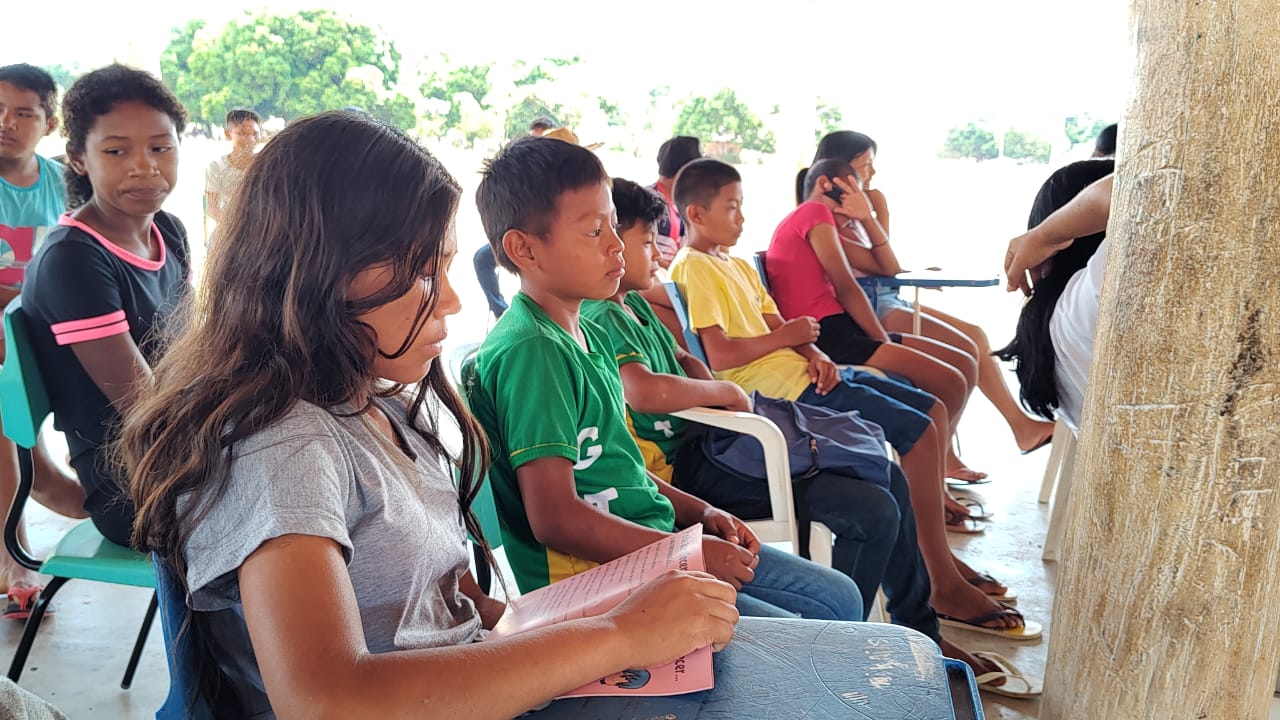 foto colorida dando enfoque em uma adolescente indigena lendo a cartilha da ouvidoria