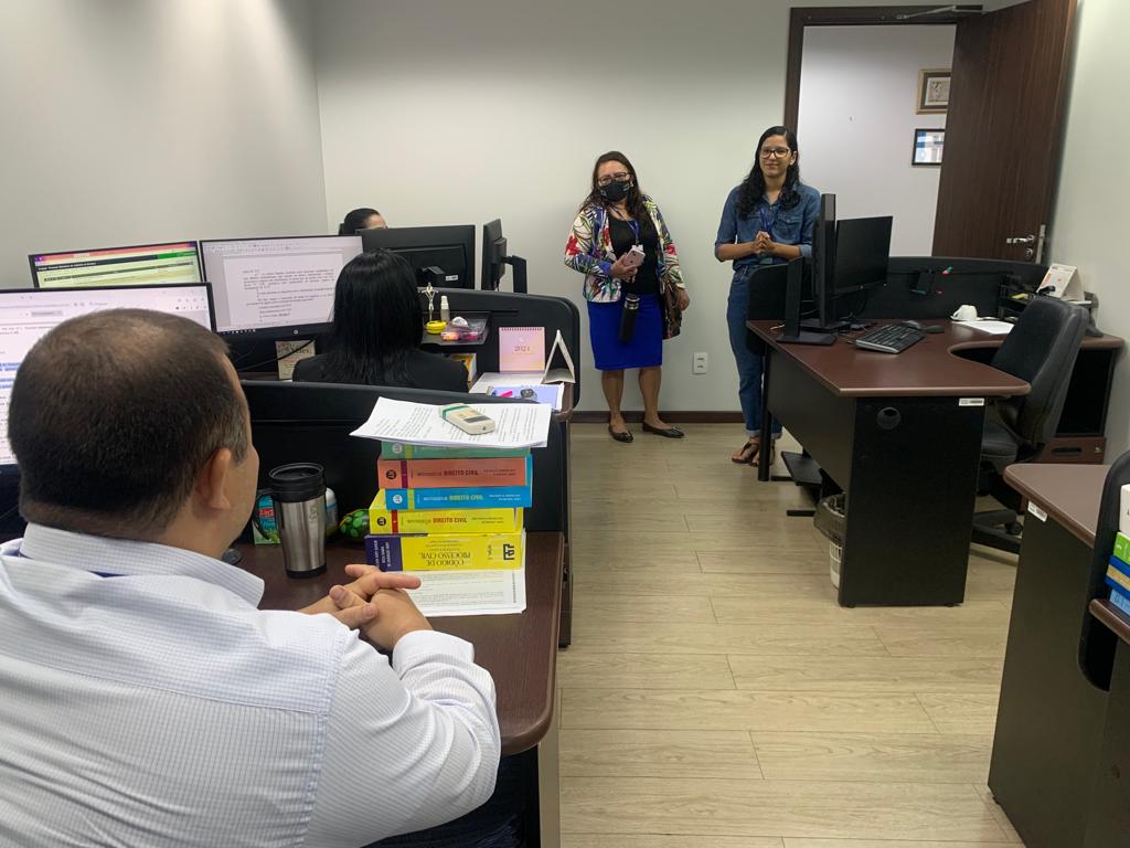  Foto colorida mostra quatro mulheres em uma sala. Duas estão em pé, e outras duas sentadas de frente para alguns monitores.