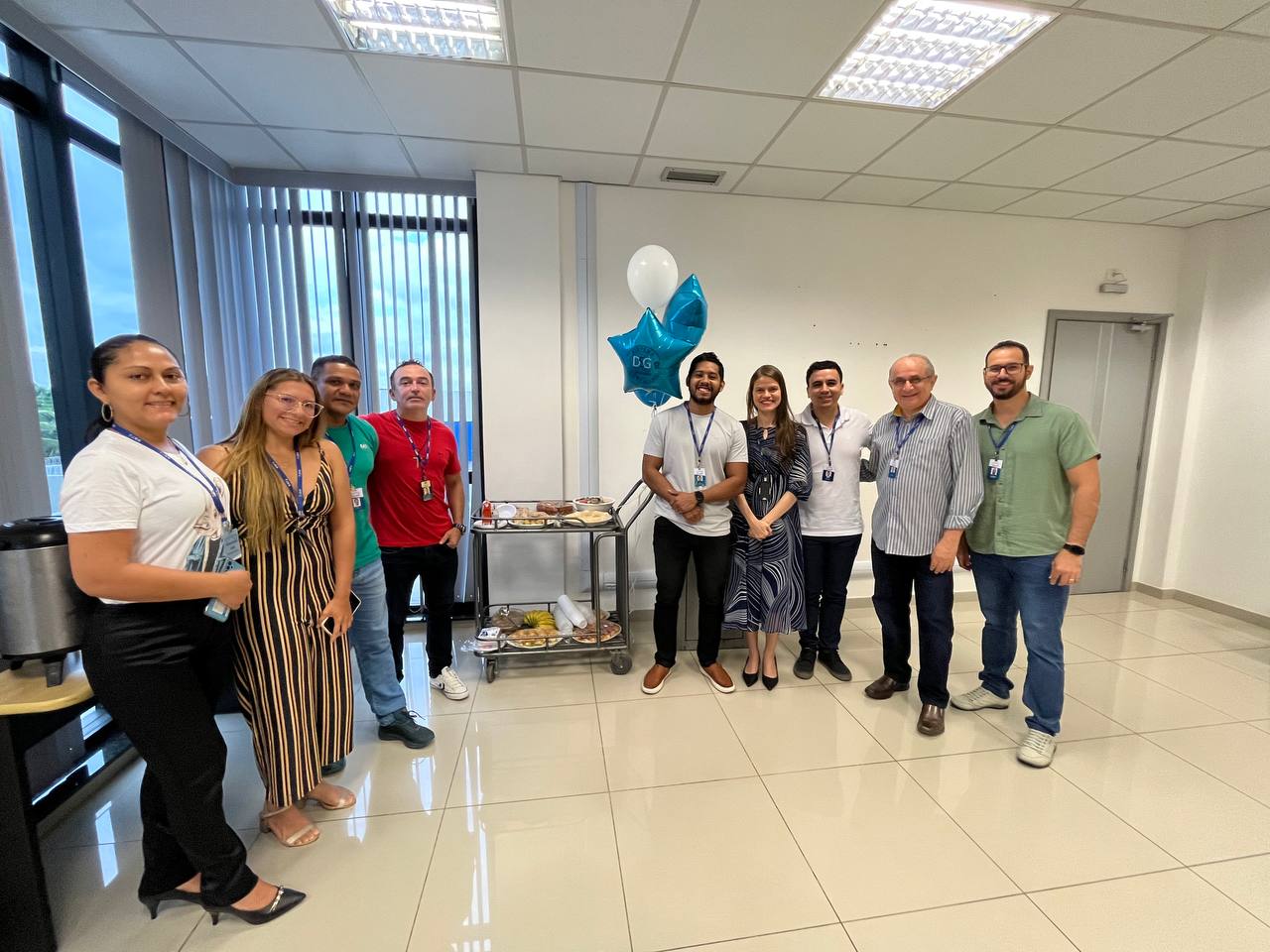 foto colorida de servidores do Tjrr pousando para a foto e ao meio há um carrinho de metal com o lanche e balões azul e branco pendurado