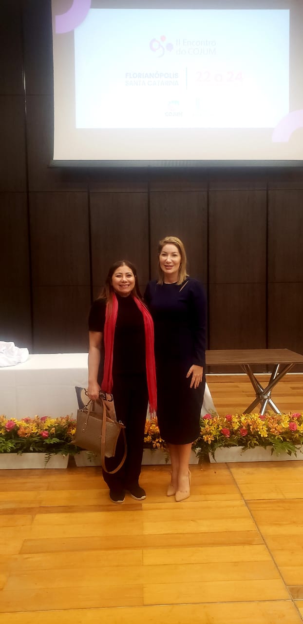 Foto colorida de duas mulheres pousando para a fotografia em pé