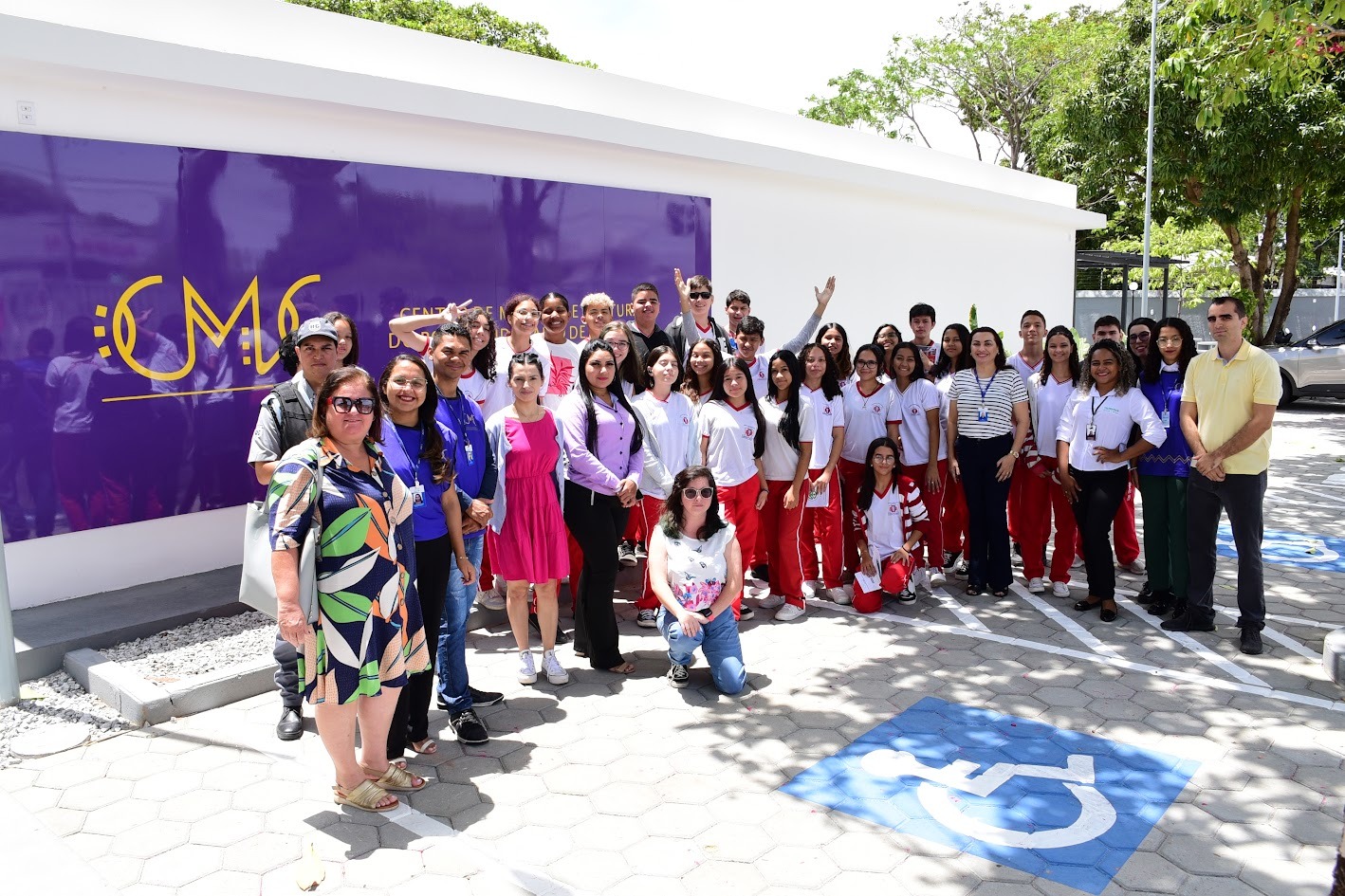 Foto colorida mostrando estudantes do ensino fundamental, juntamente com gestores e professores, além de servidores do Centro de Memória e Cultura, posando para foto em frente a fachada do prédio.